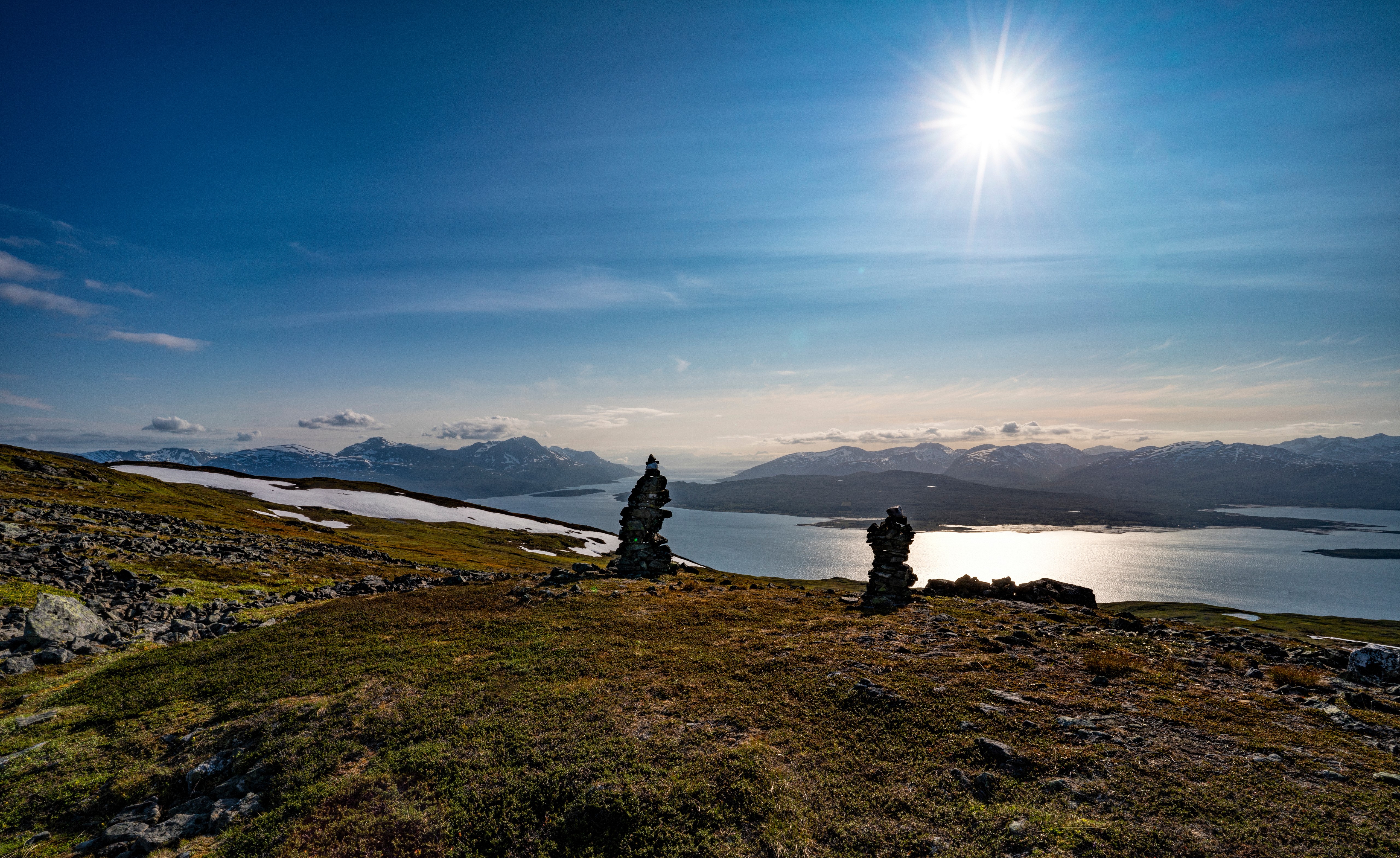 Two stone cairns on a grassy hill overlooking a fjord HD Wallpaper