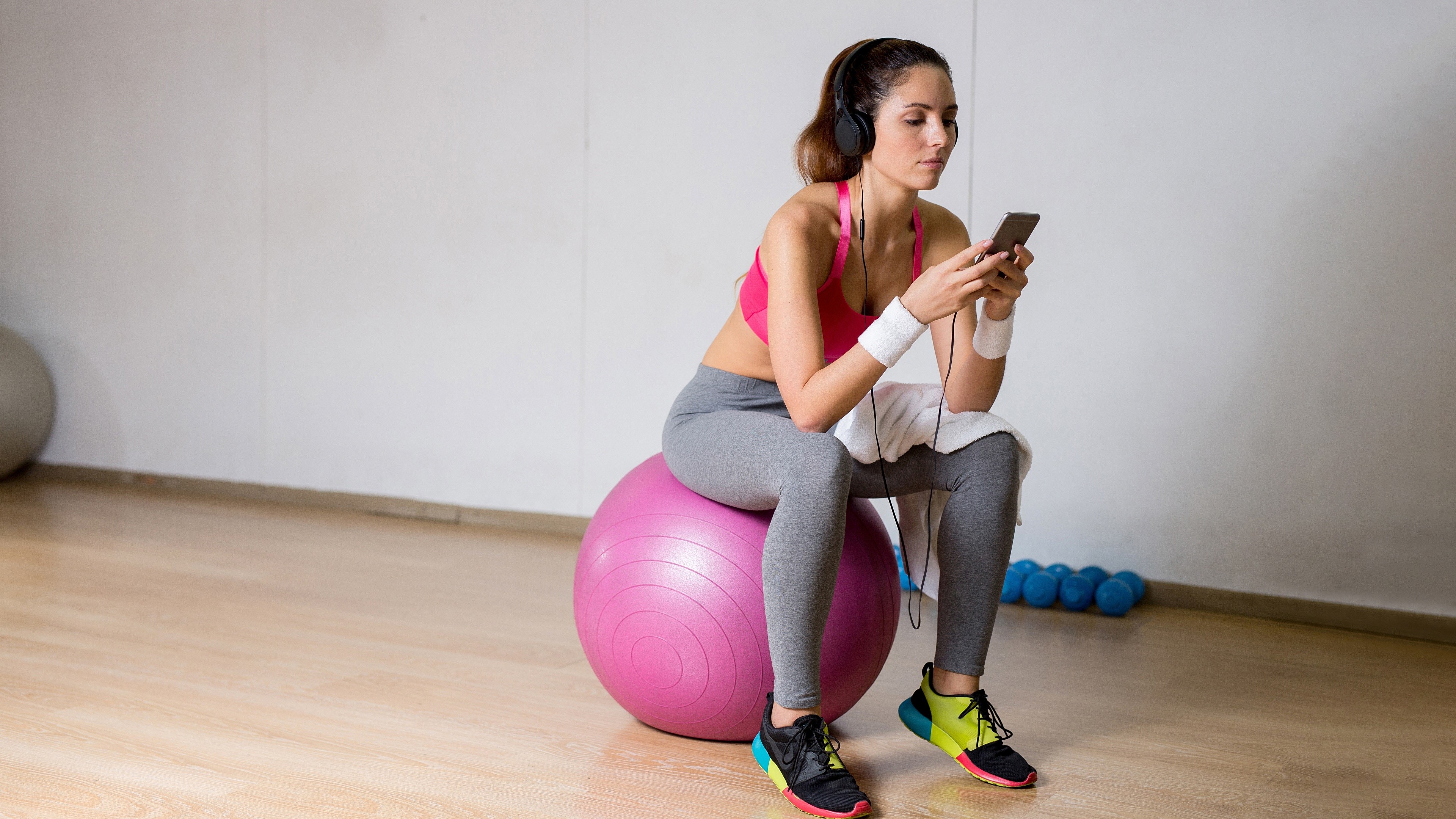 Woman in headphones sitting on fitness ball with smartphone HD Wallpaper