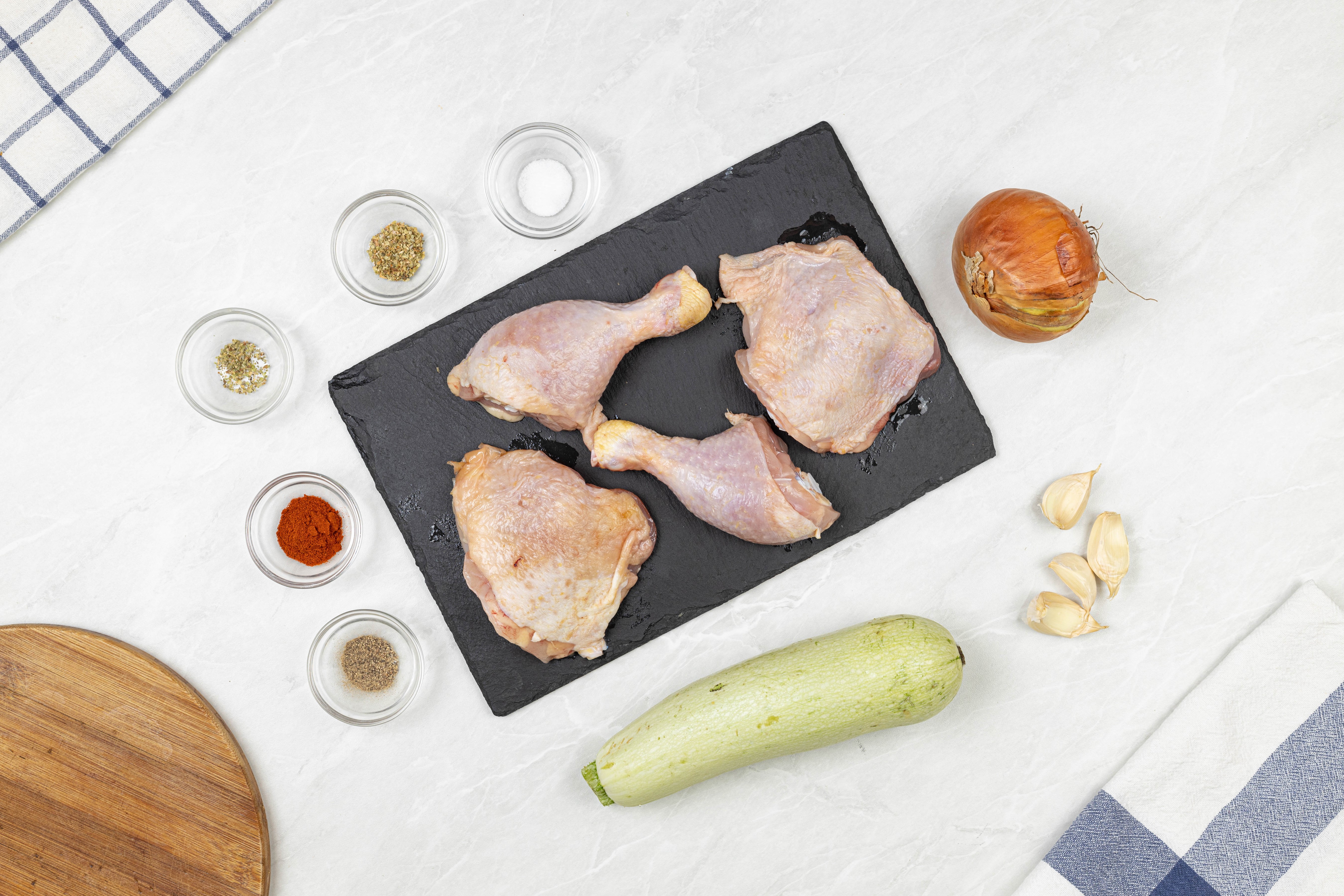 Raw chicken legs and thighs with zucchini, onion, garlic, and spices HD Wallpaper