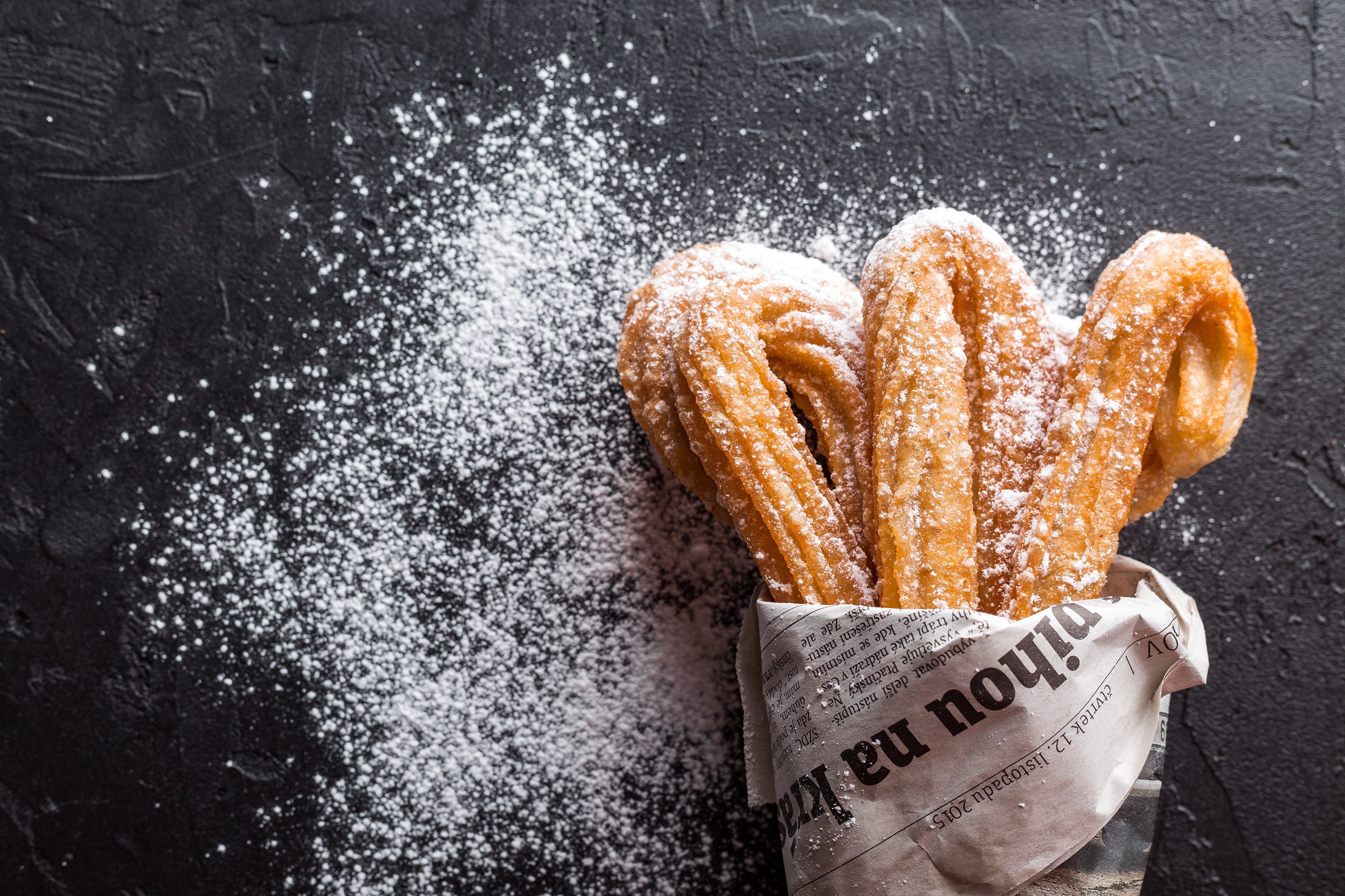 Churros with powdered sugar on newspaper HD Wallpaper
