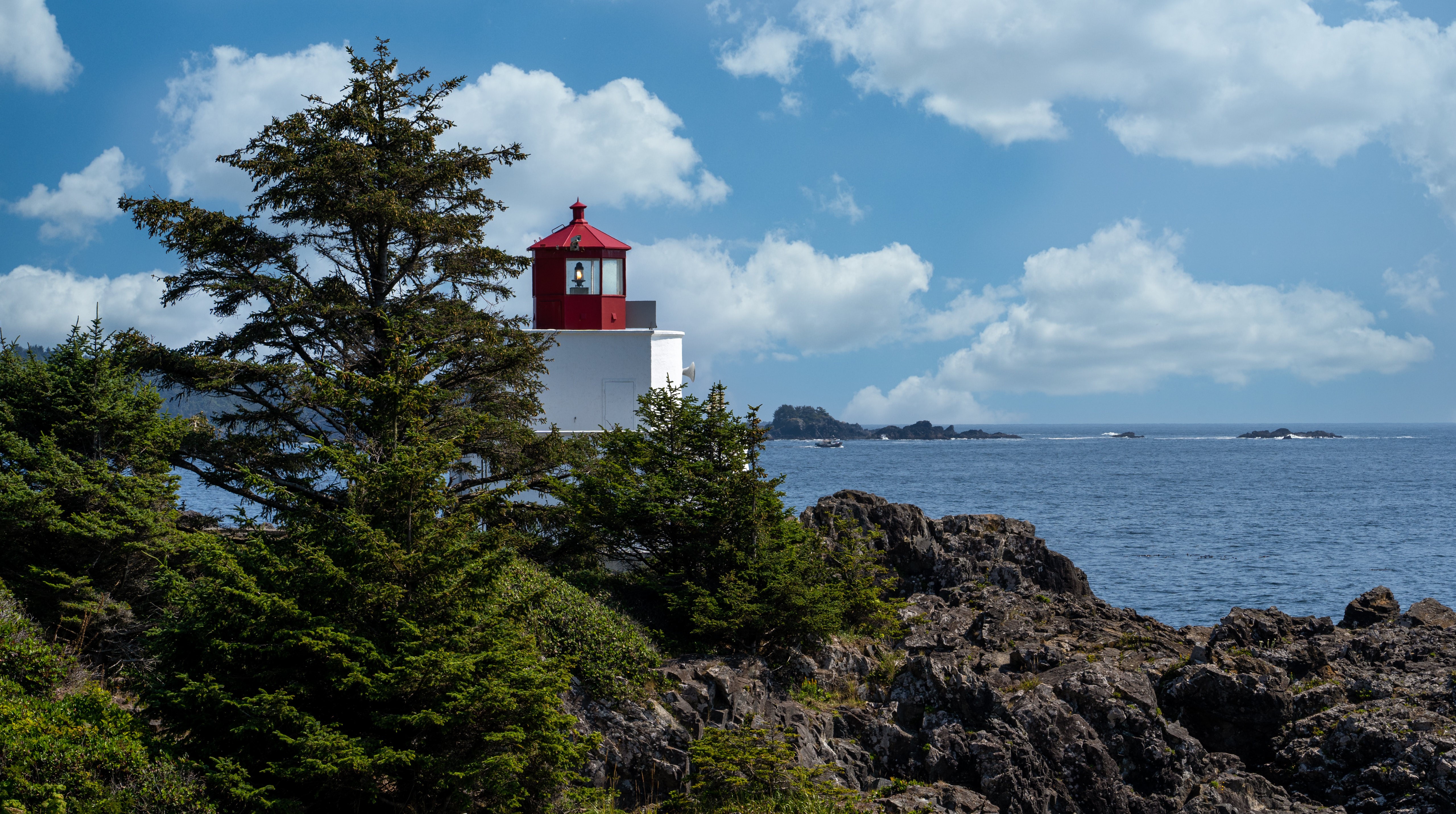 Lighthouse on a rocky coast with trees and clouds HD Wallpaper
