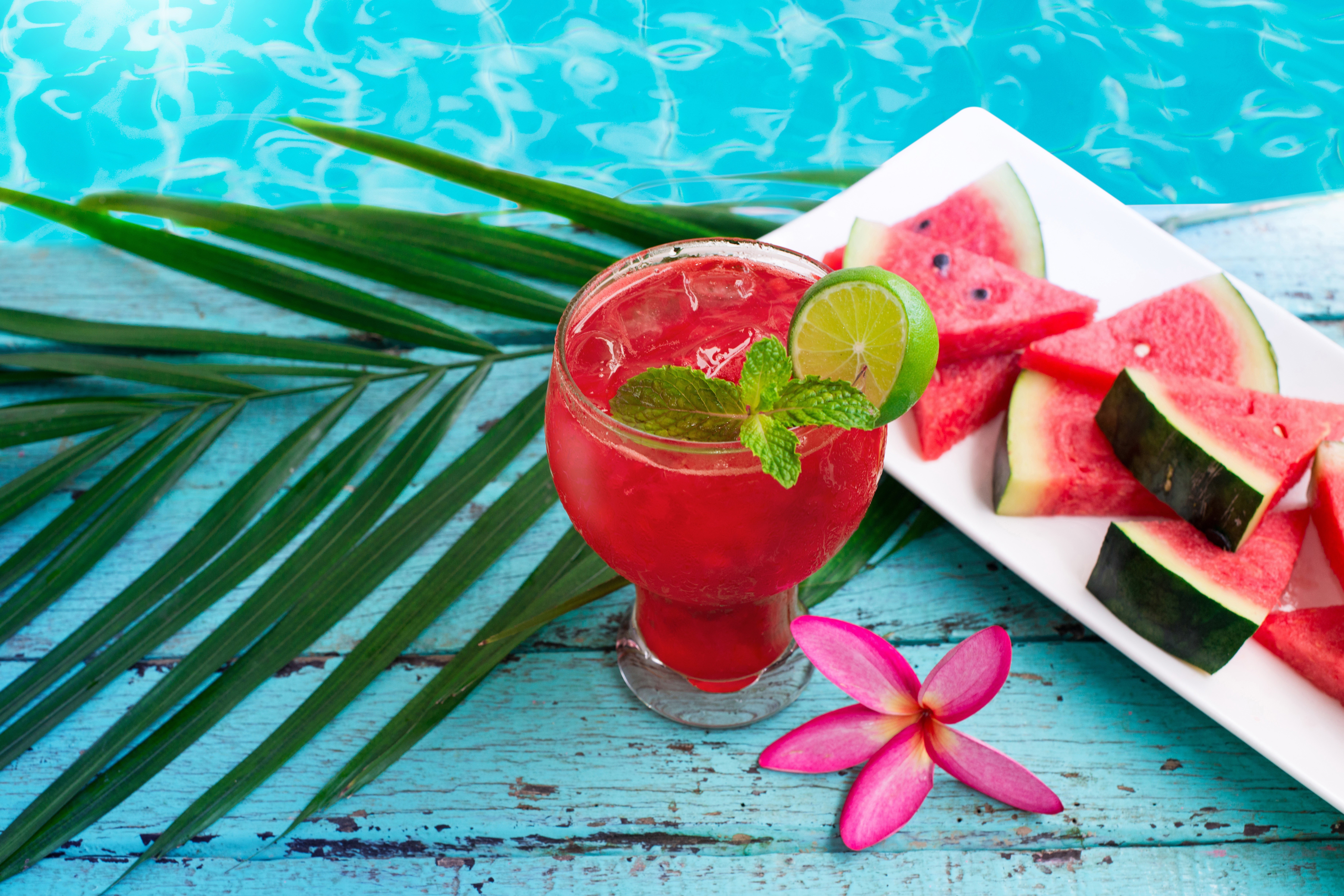Watermelon juice with watermelon slices and palm leaves by the pool HD Wallpaper