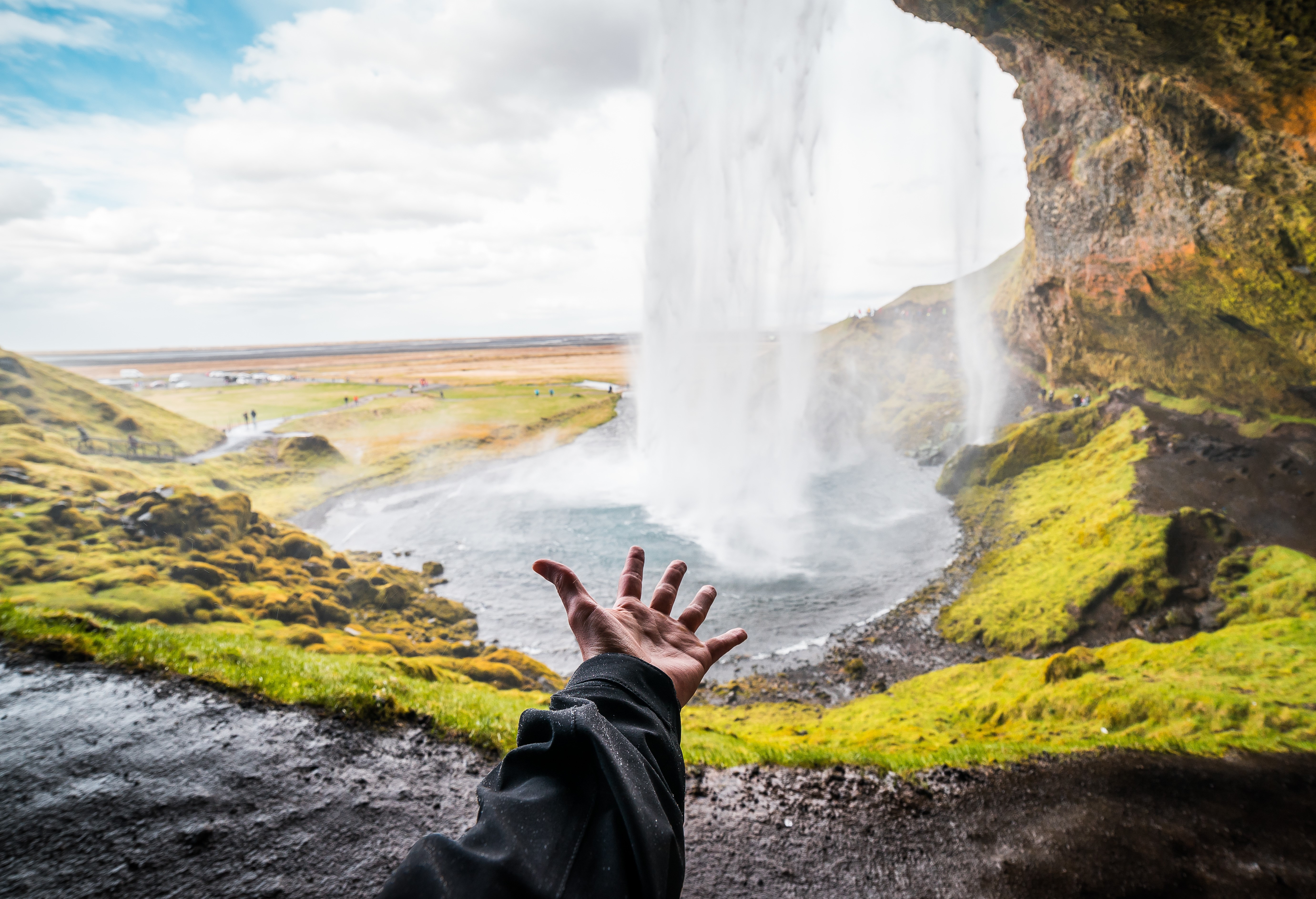 Hand reaching out towards Seljalandsfoss waterfall in Iceland HD Wallpaper