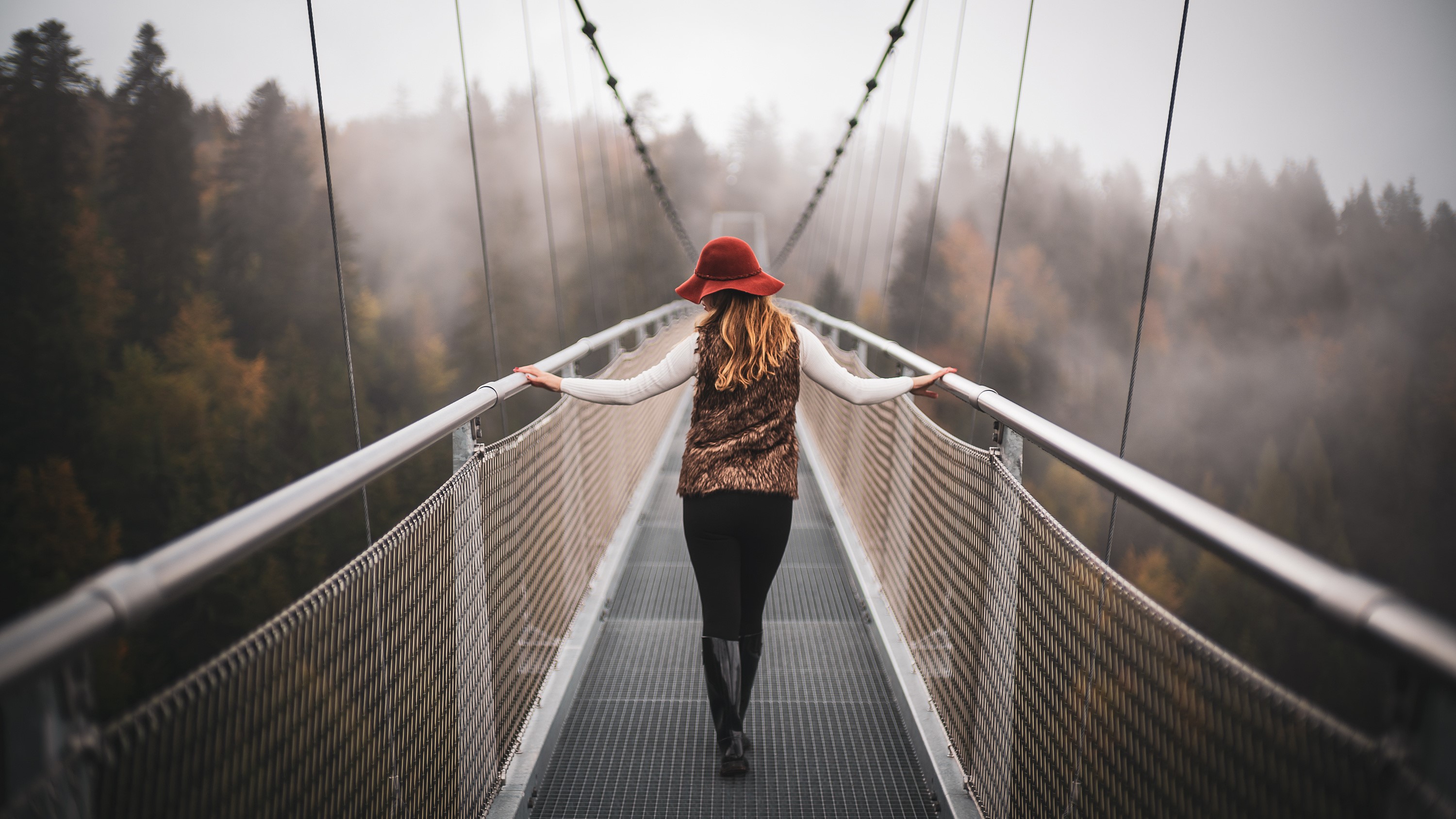 Woman in hat walking on a foggy suspension bridge in Switzerland HD Wallpaper