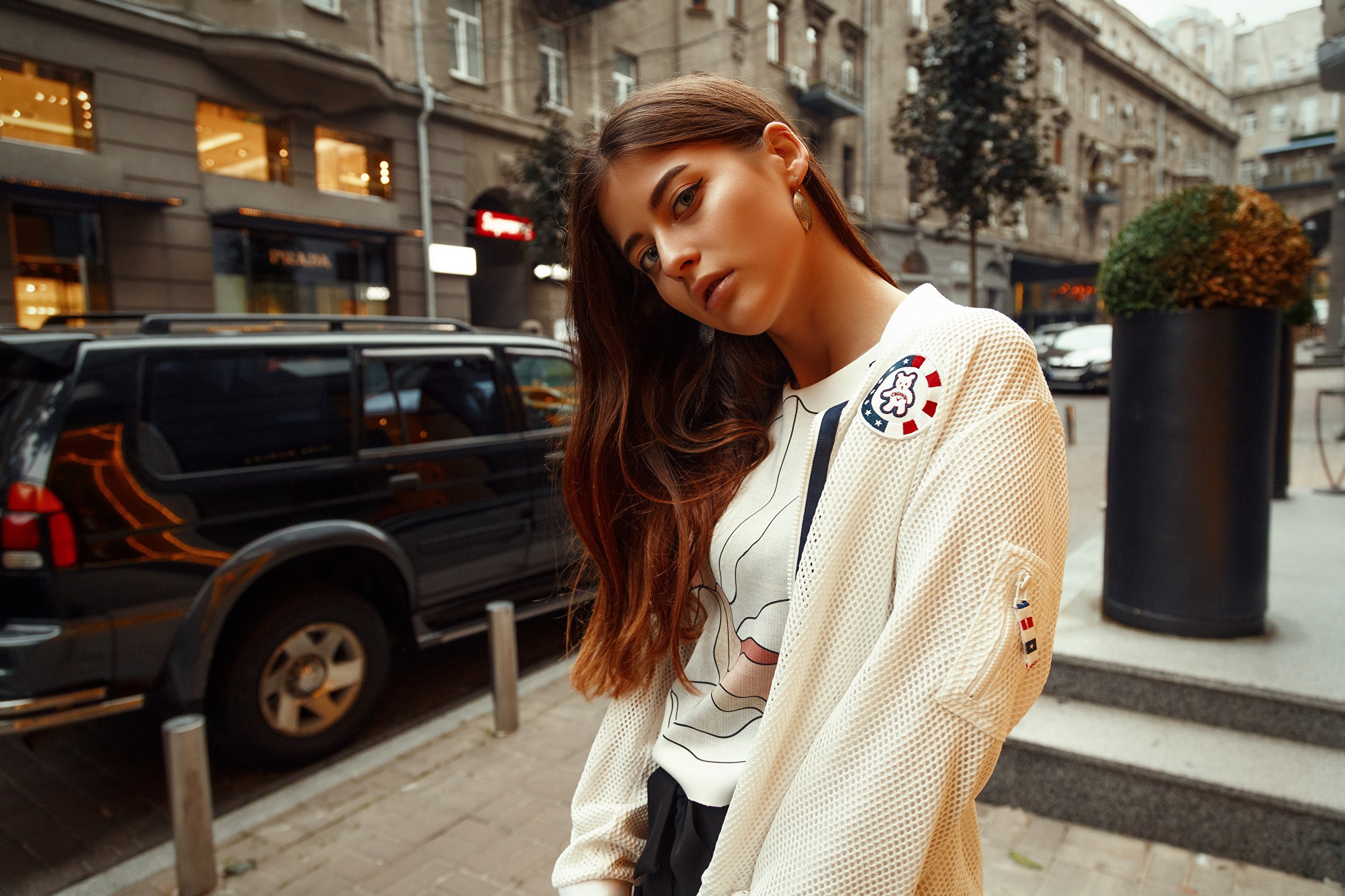 Woman with brown hair in a white jacket on a city street HD Wallpaper