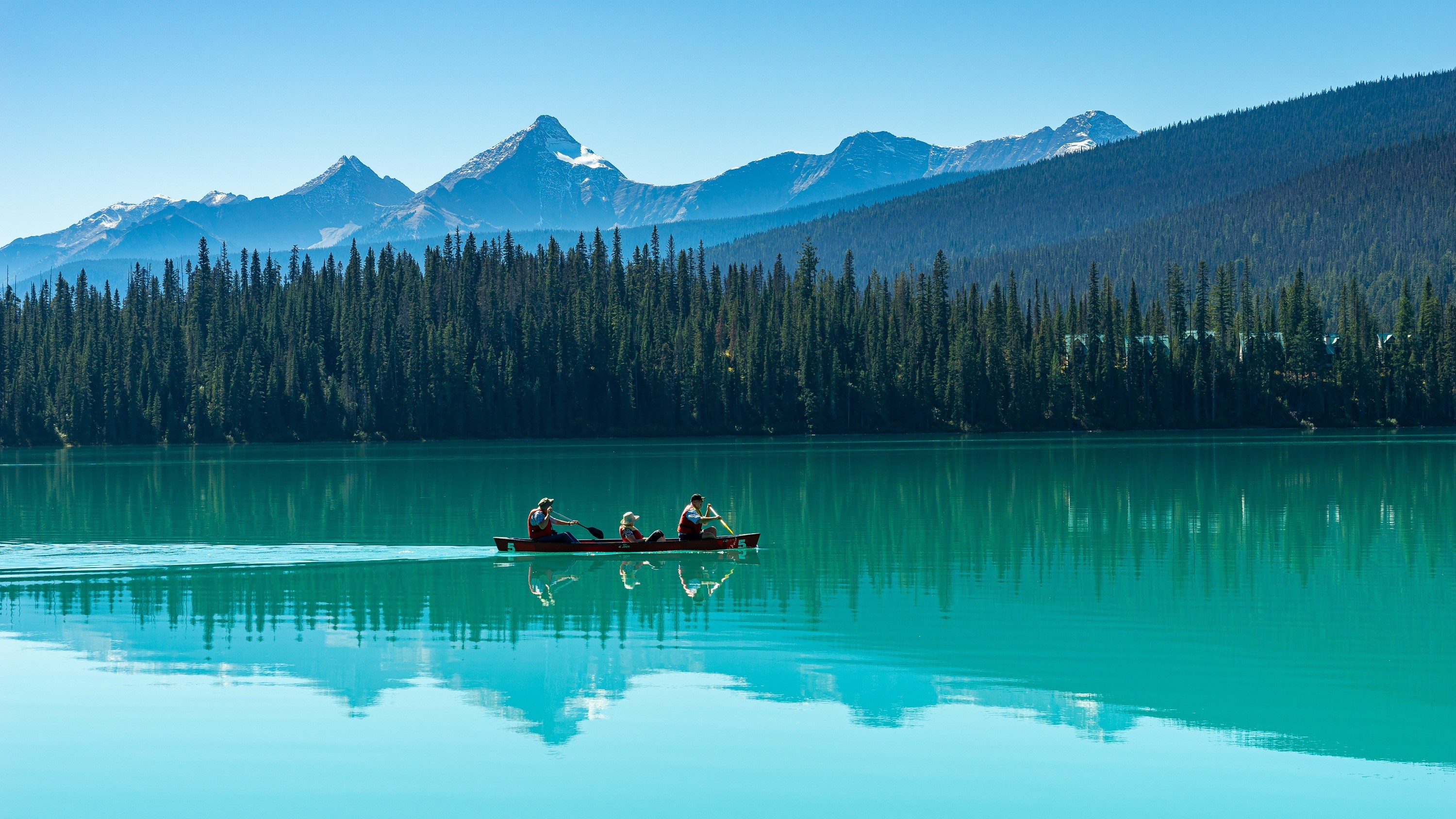 Canoeists on a turquoise lake with mountains and forest HD Wallpaper