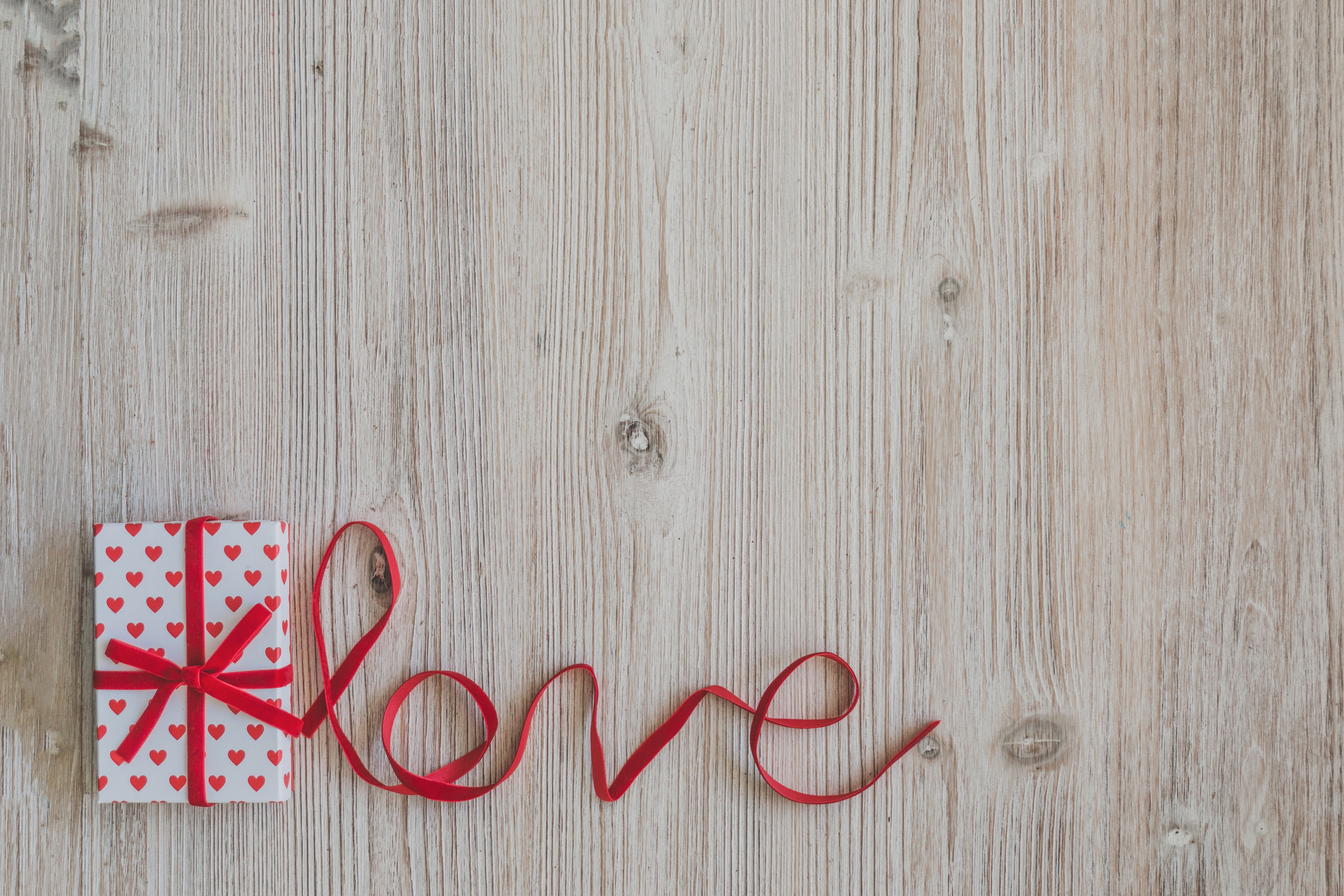 Gift with red ribbon spelling "Love" on wooden background HD Wallpaper