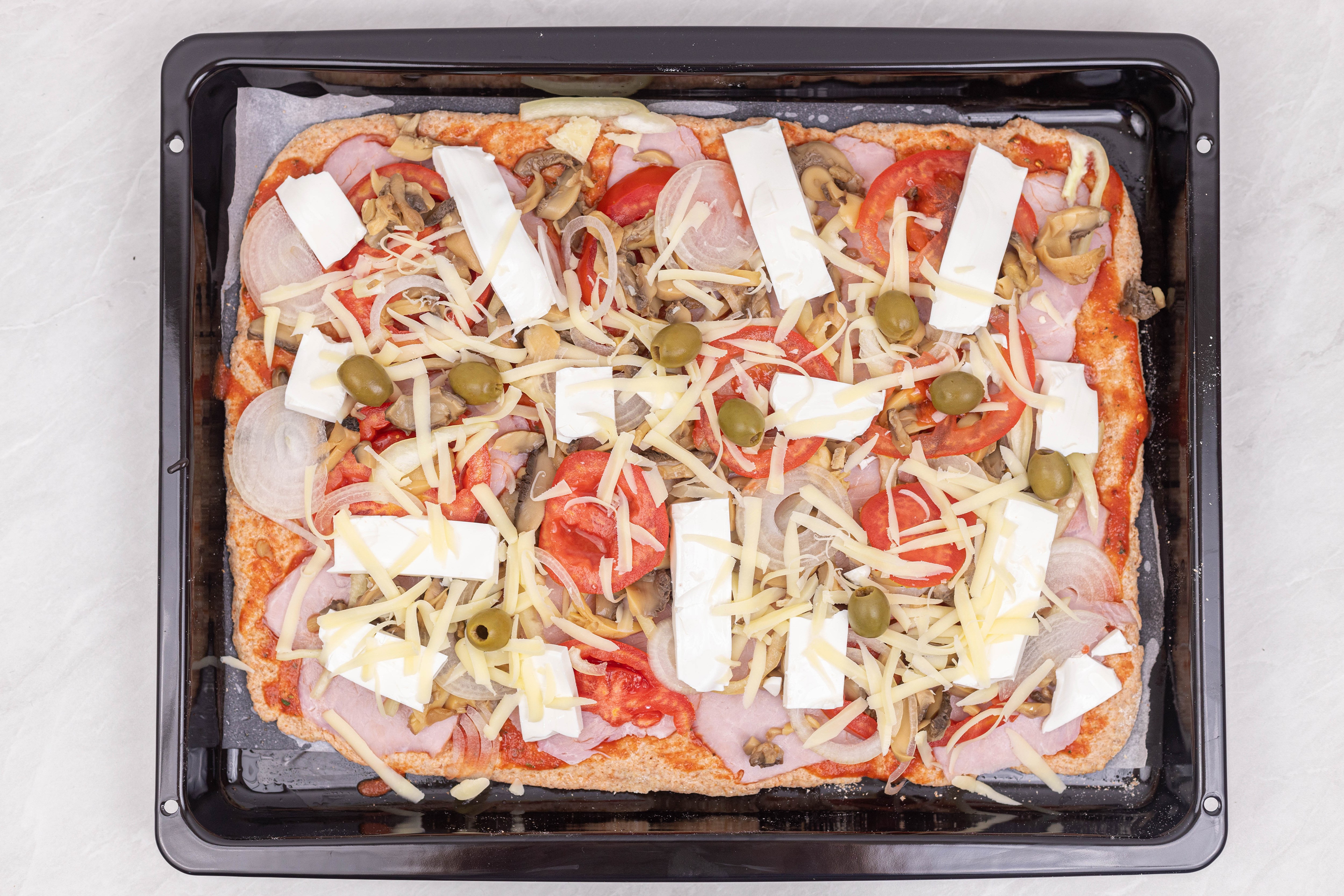 Rectangular pizza with ham, mushrooms, tomatoes, onions, olives, and cheese on a baking sheet HD Wallpaper