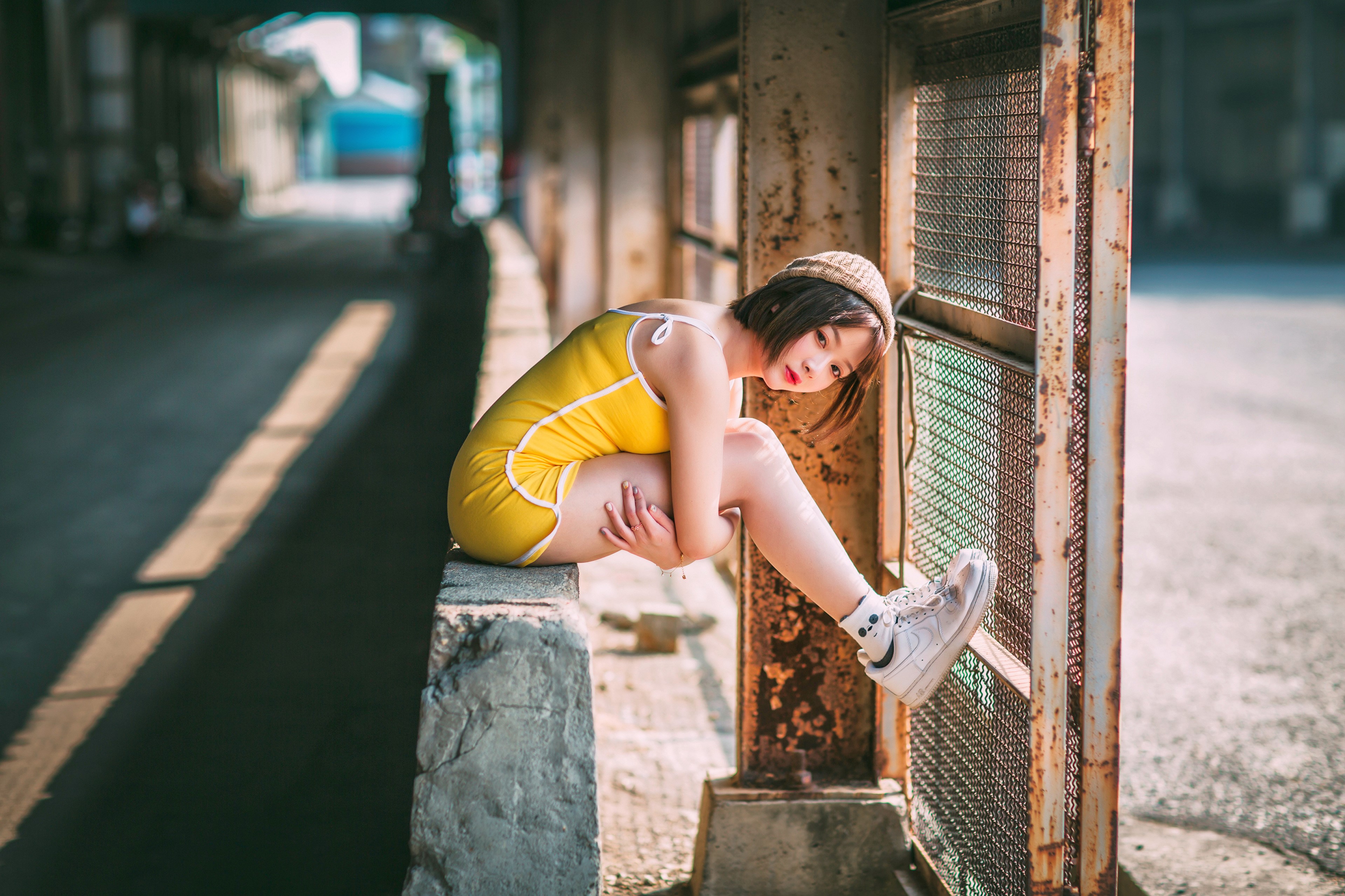 Asian girl in yellow outfit sitting by rusty fence HD Wallpaper