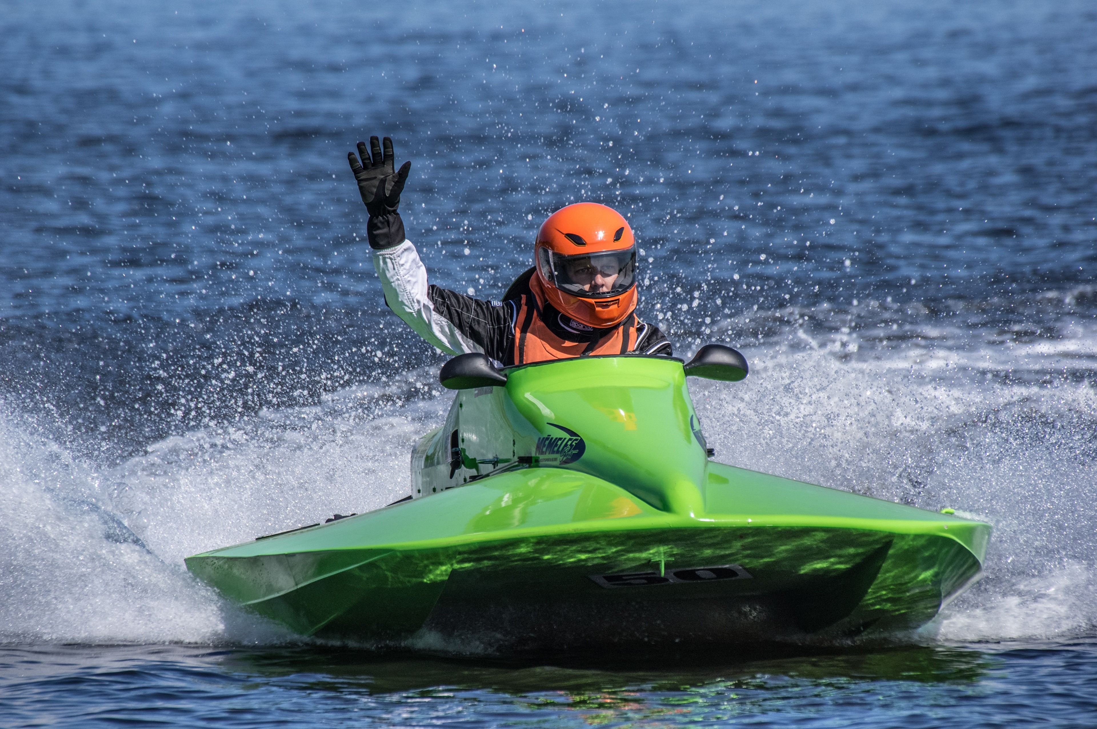 Person in green watercraft wearing orange helmet waving HD Wallpaper