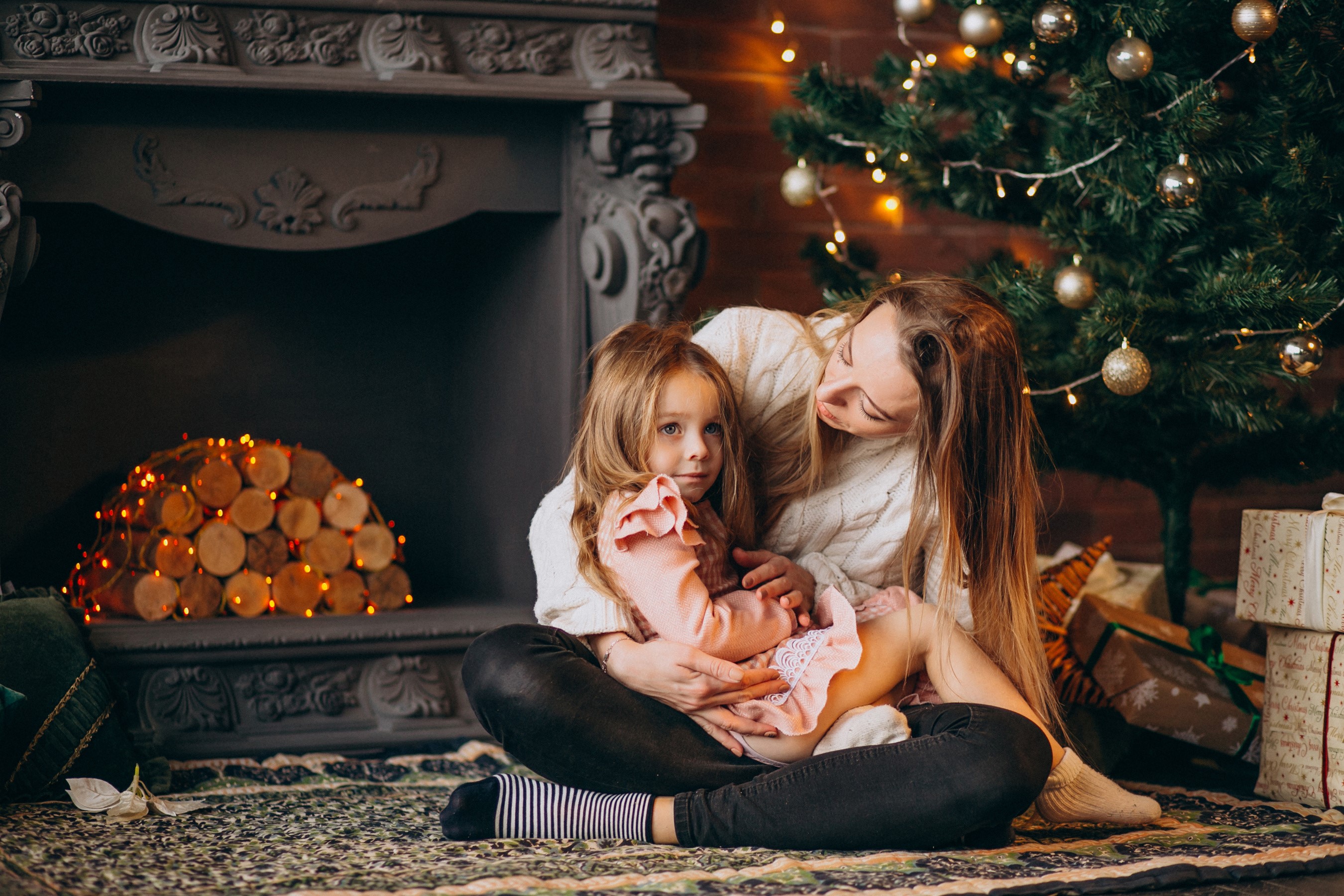 Mother and daughter by a Christmas tree and fireplace HD Wallpaper