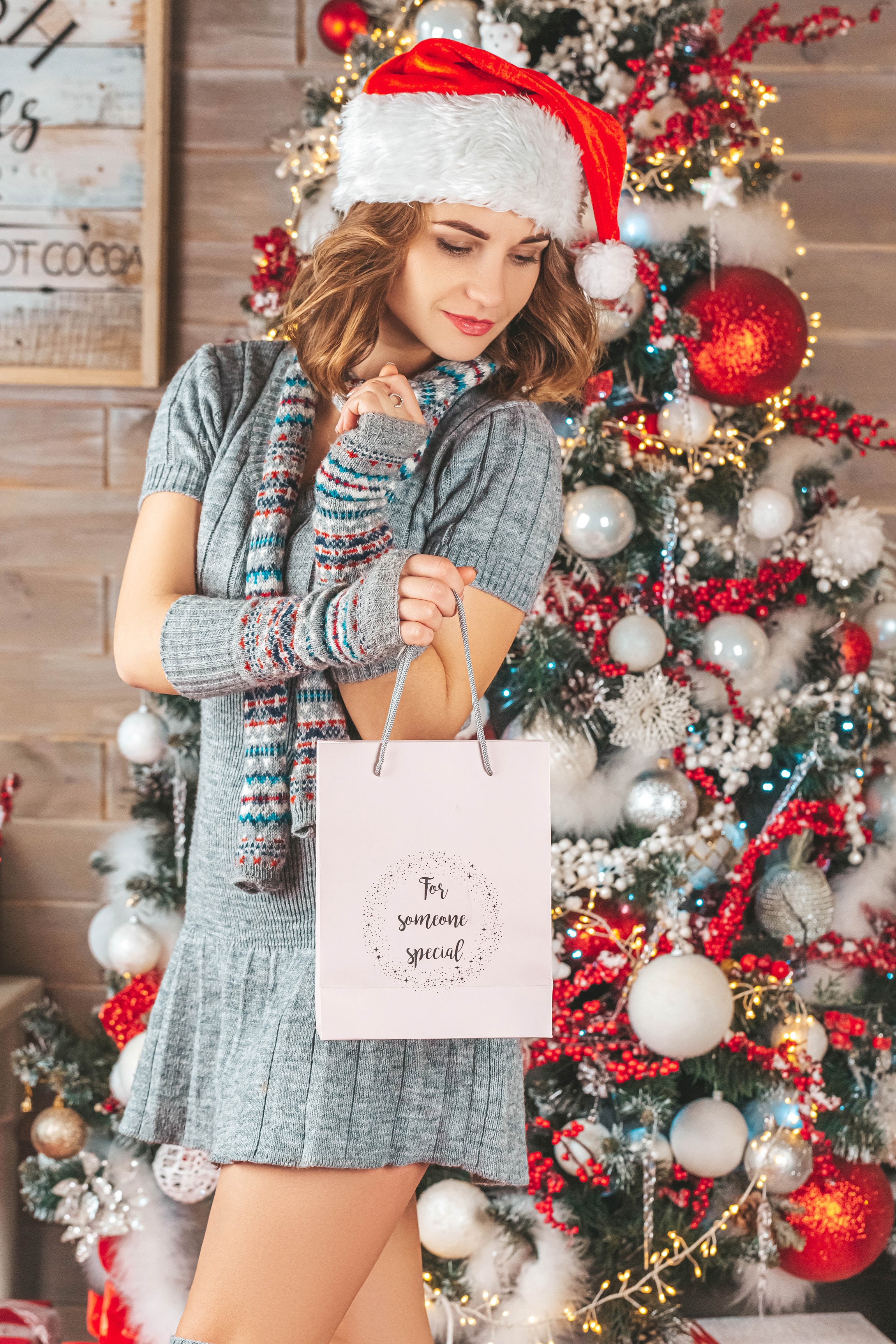 Woman in Santa hat holding gift bag by Christmas tree HD Phone Wallpaper