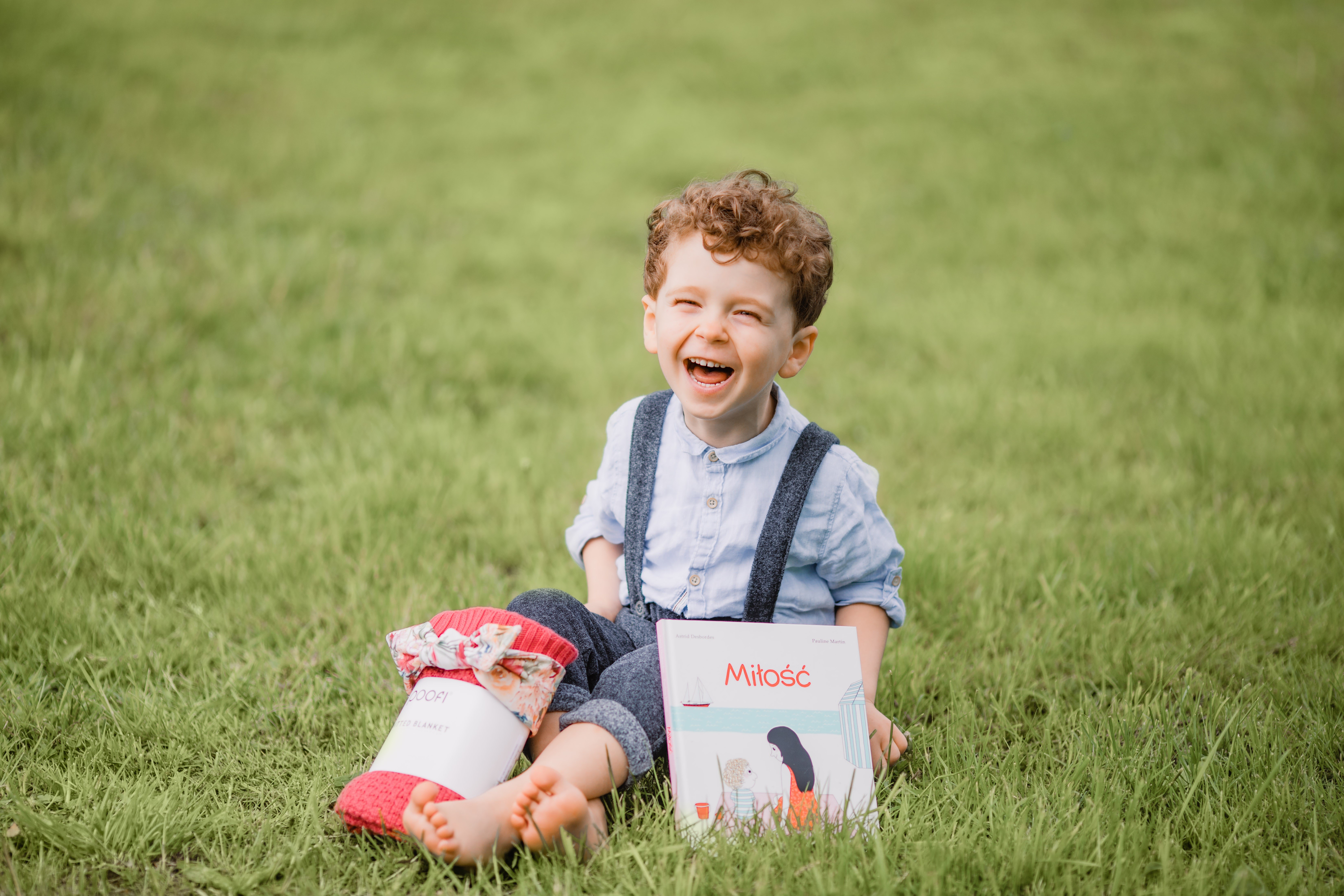 Boy laughing with a book and blanket on grass HD Wallpaper