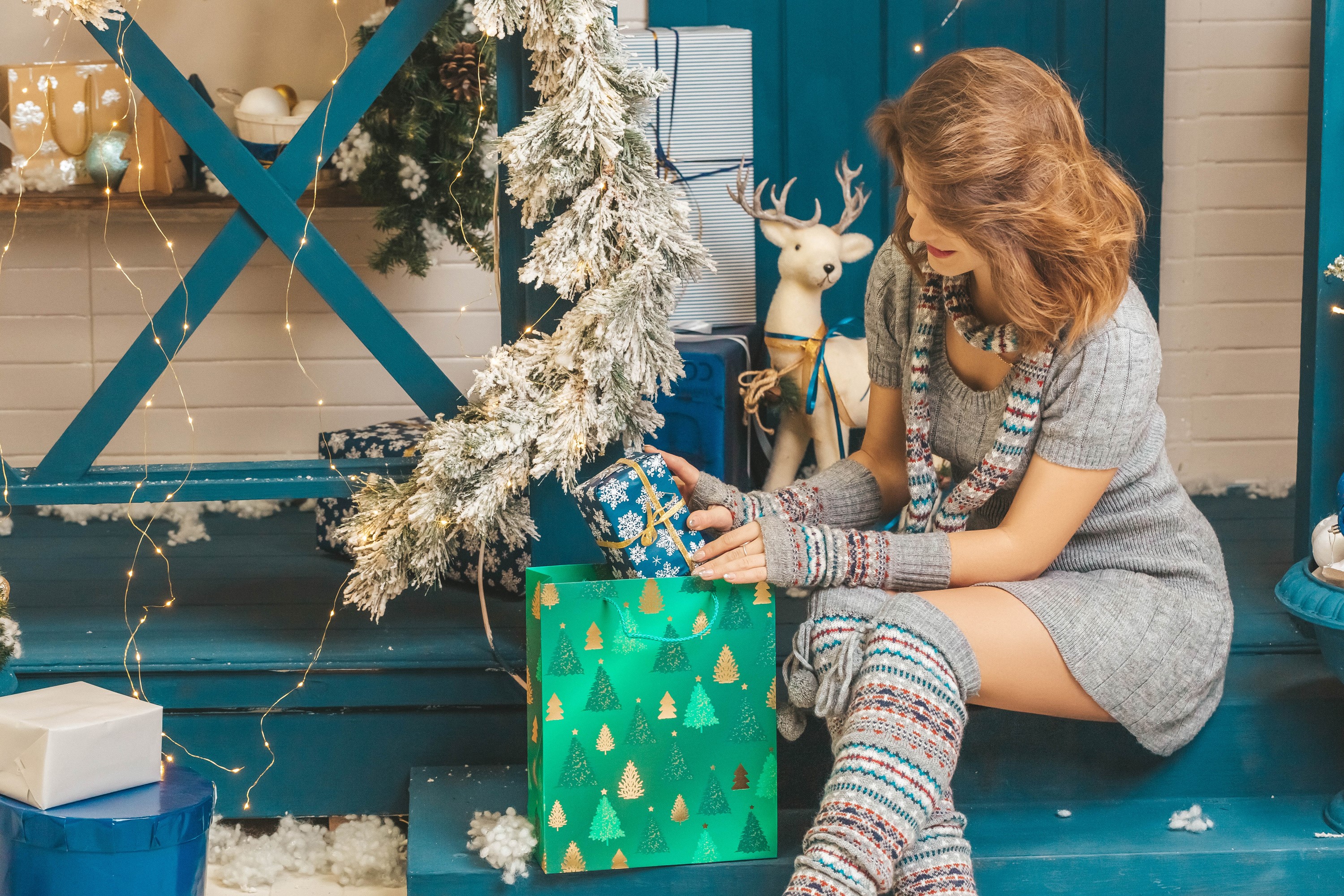Woman opening Christmas gifts with fairy lights and reindeer decoration HD Wallpaper