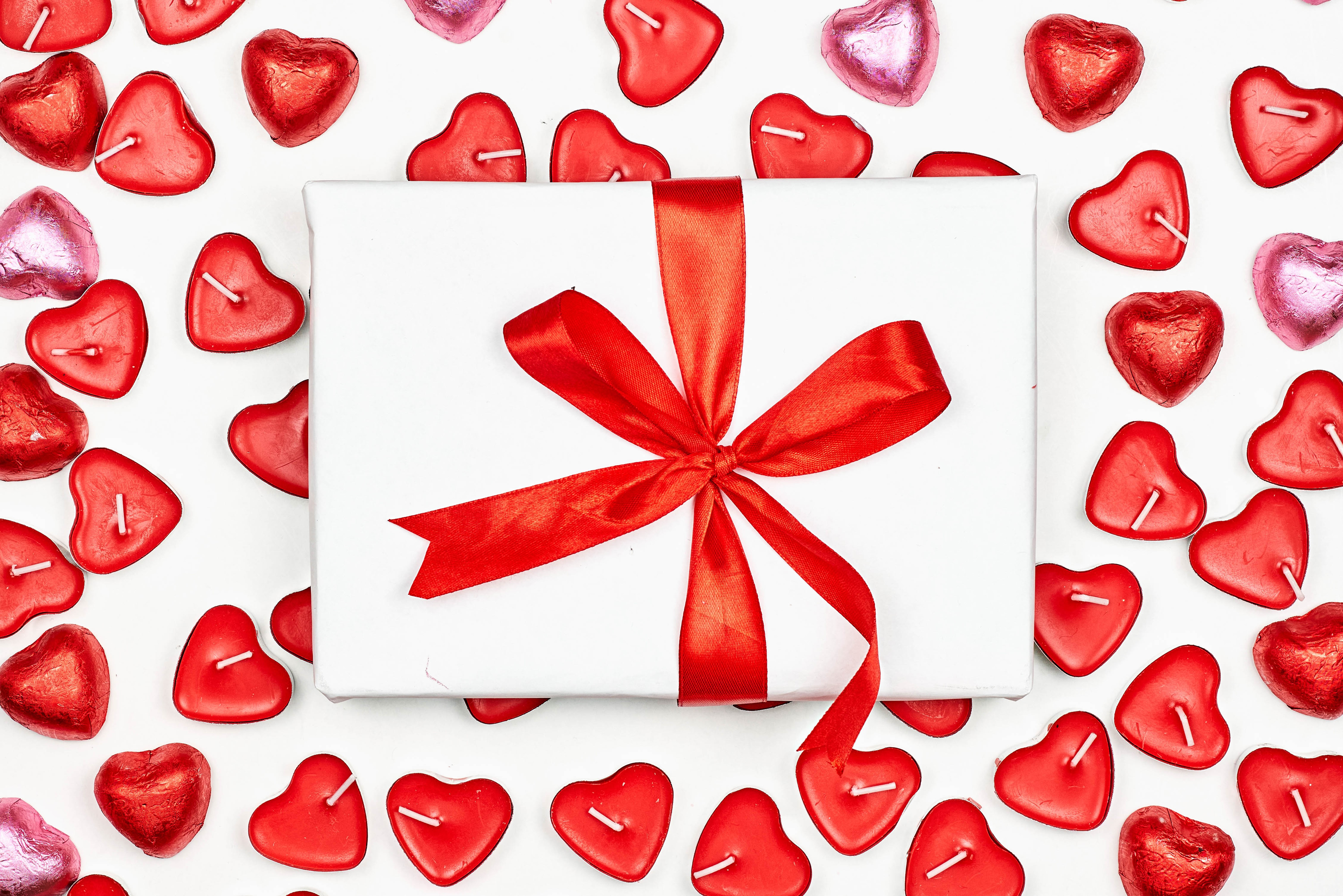 Gift box with red ribbon surrounded by heart-shaped candles HD Wallpaper