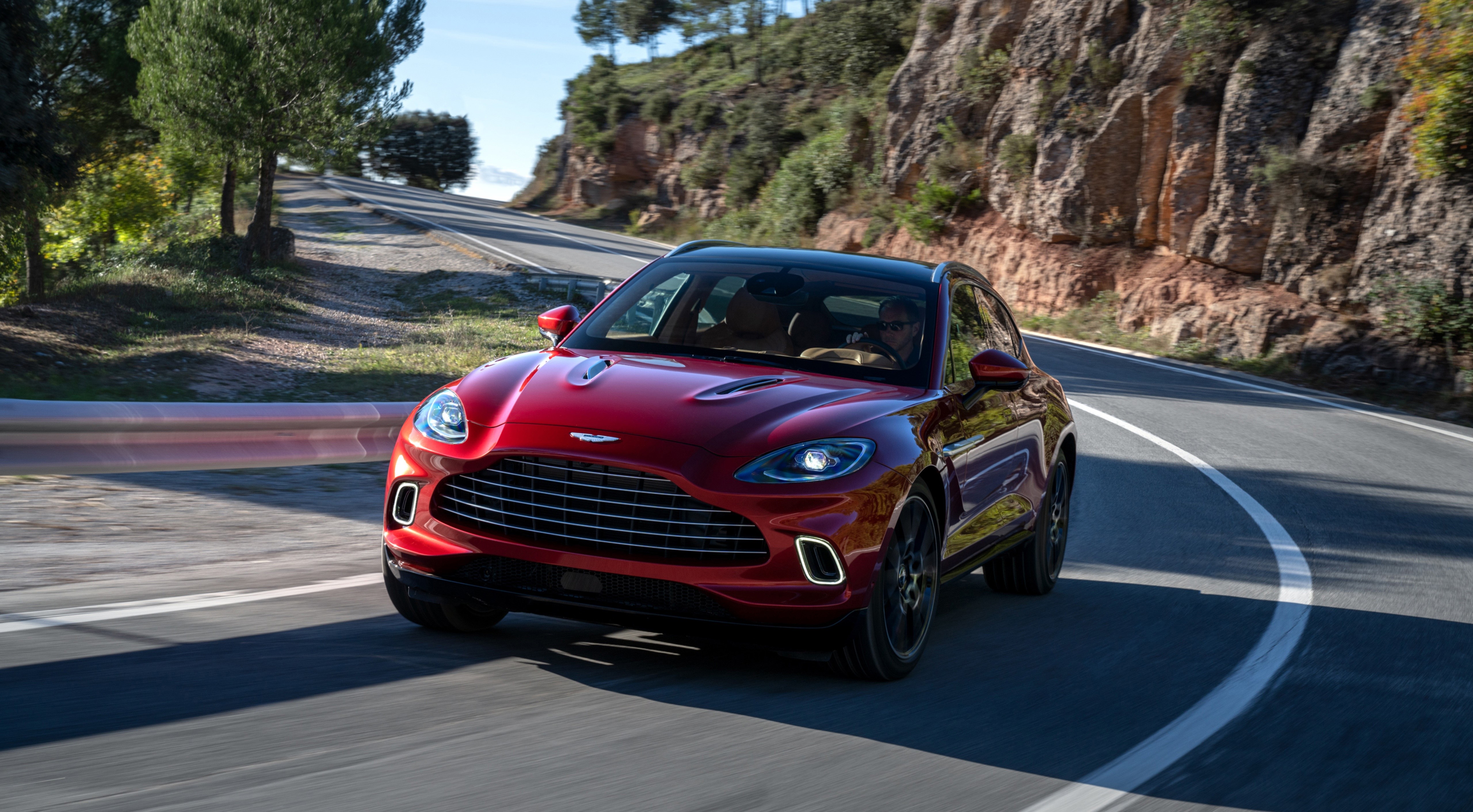 Red Aston Martin DBX driving on a winding road HD Wallpaper