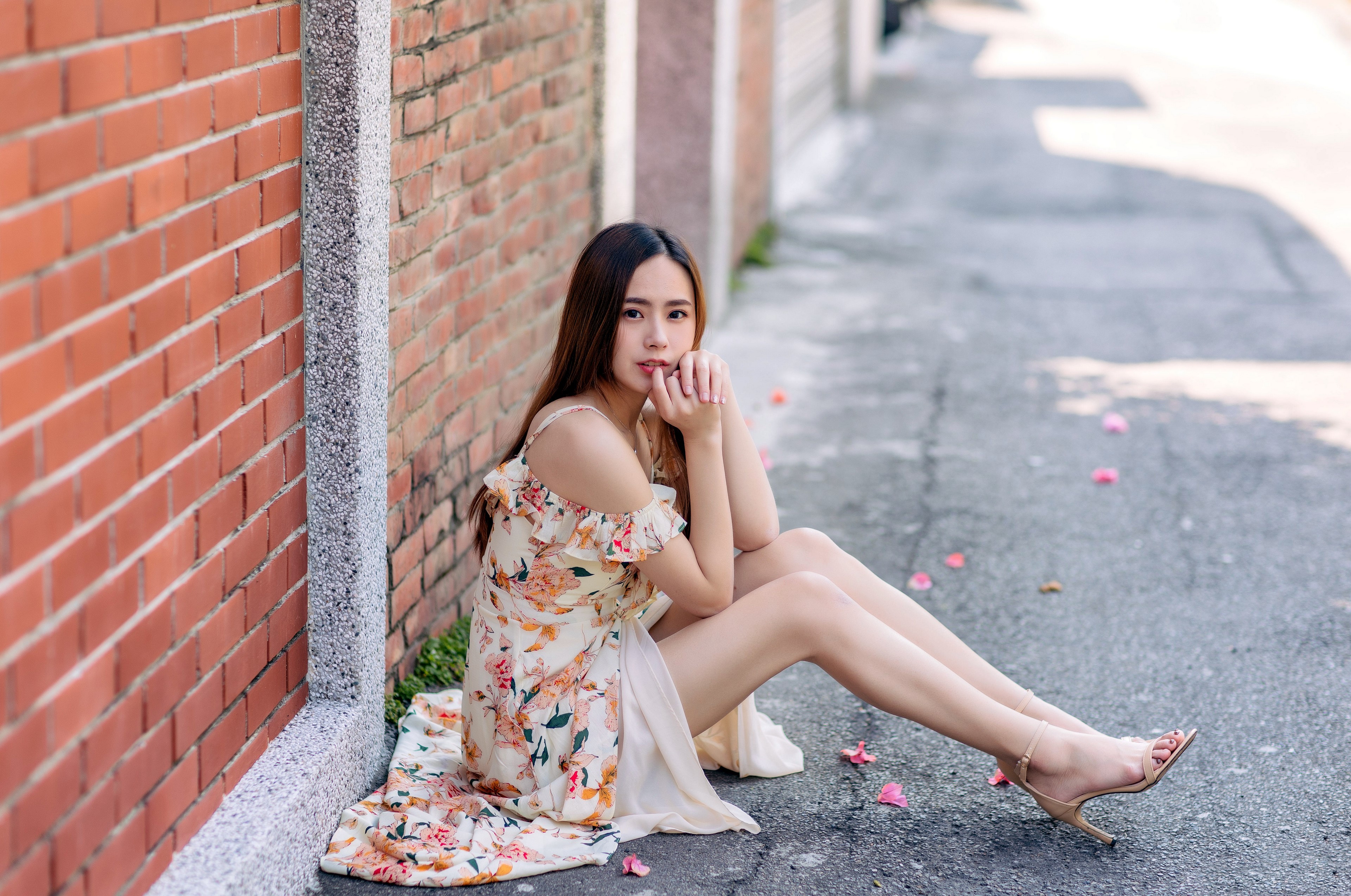 Asian woman in floral dress sitting by brick wall HD Wallpaper