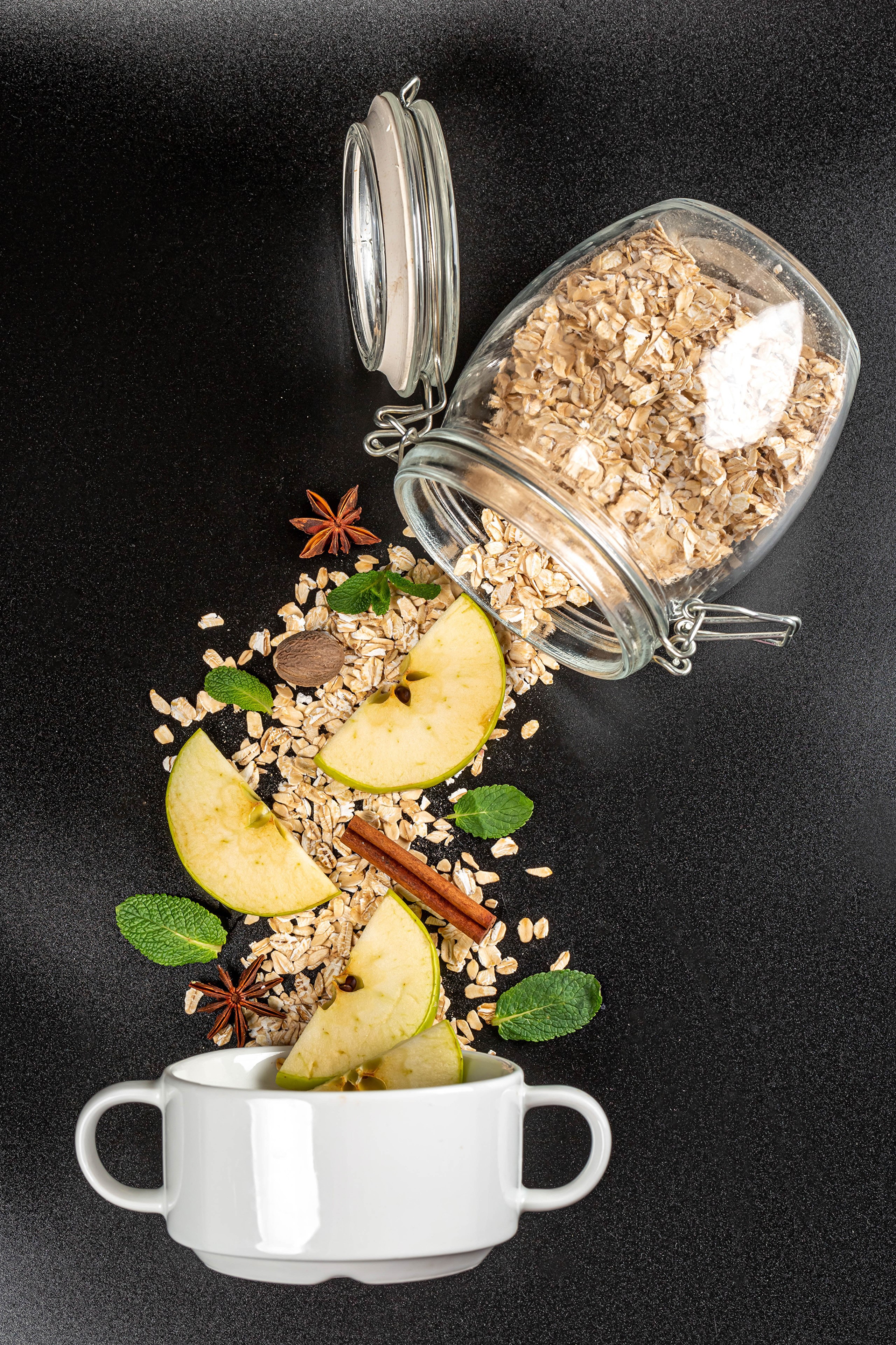 Oatmeal with apples, cinnamon, and star anise spilling from a jar into a mug HD Phone Wallpaper