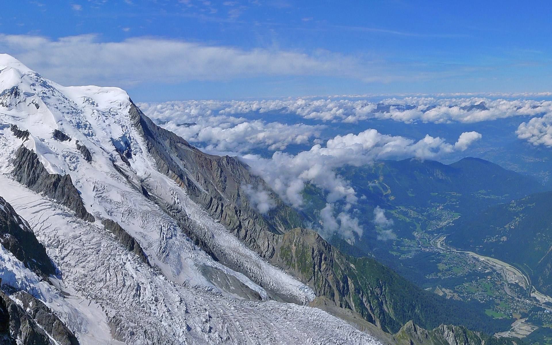 Snow-capped mountain range with clouds and valley below HD Wallpaper
