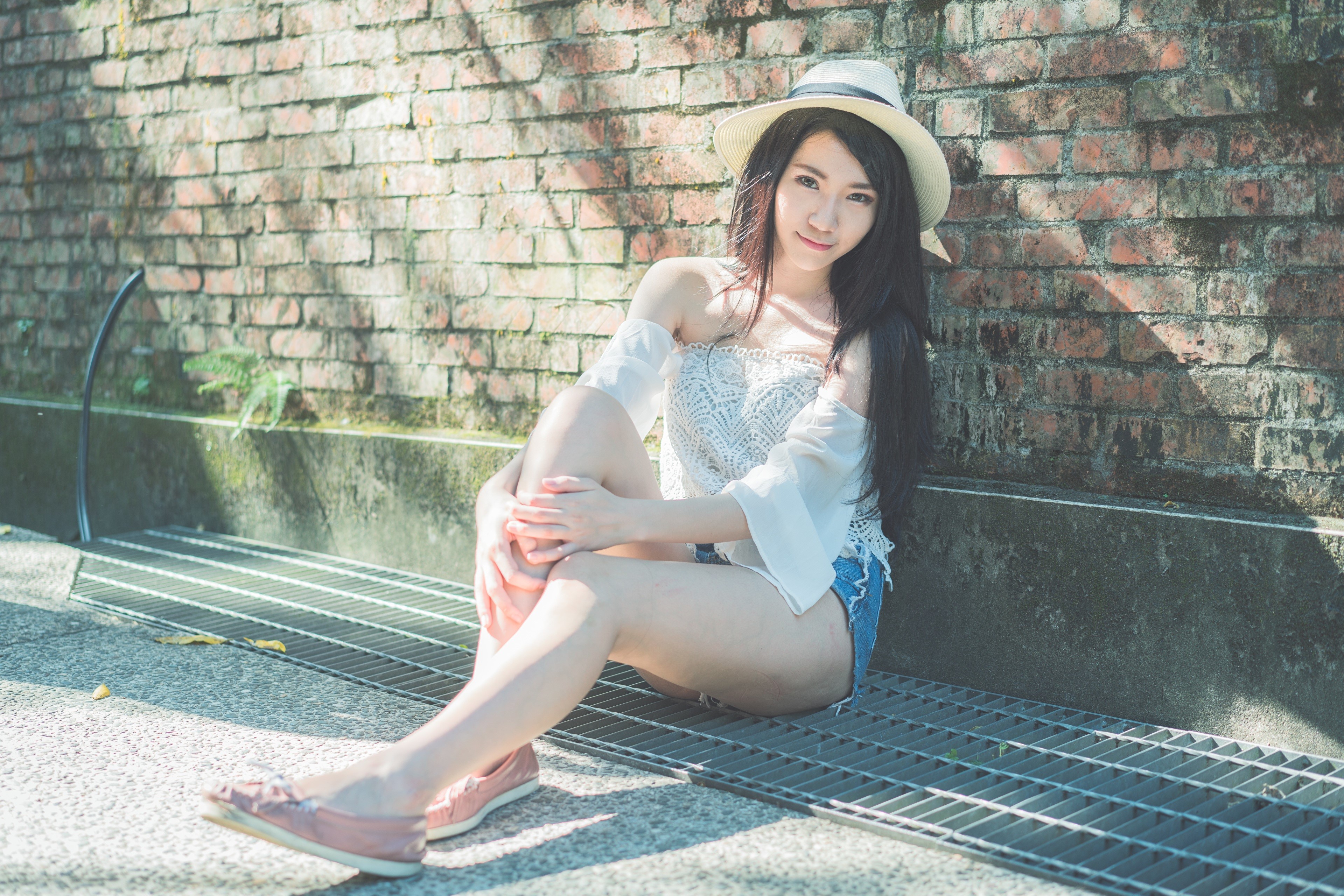 Asian girl in hat sitting by brick wall HD Wallpaper