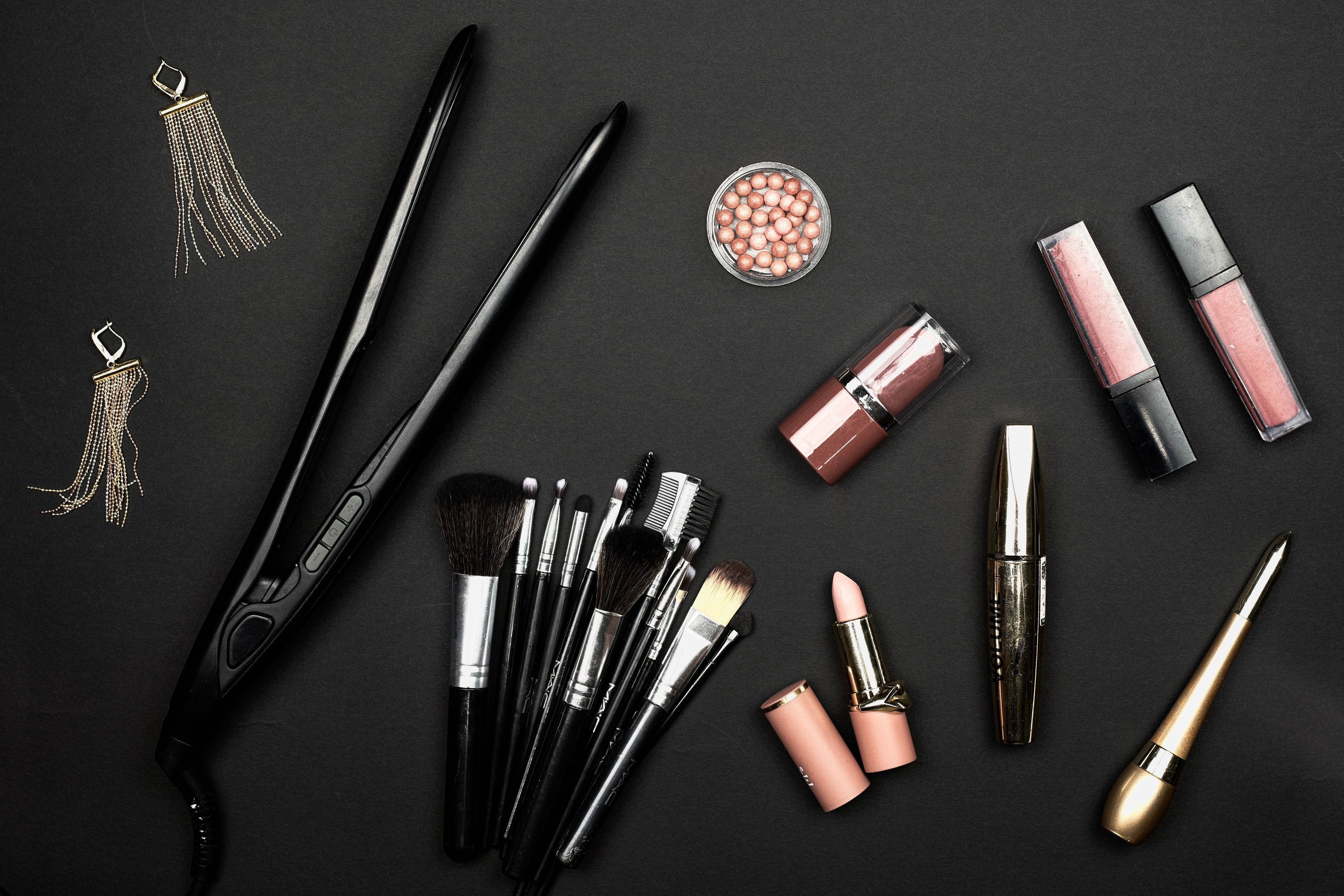Flat iron, makeup brushes, earrings, and cosmetics on black background HD Wallpaper