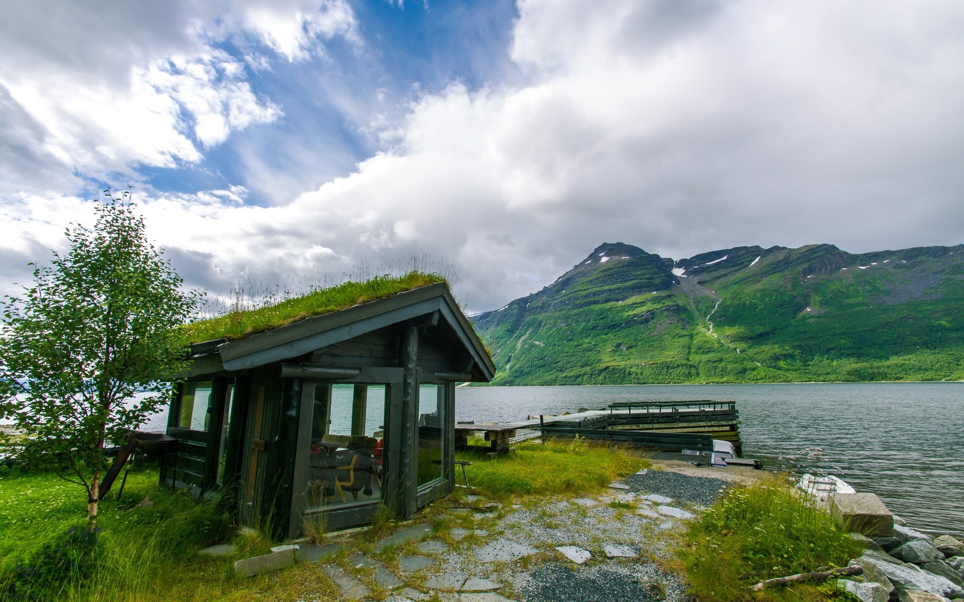 Cabin with grass roof by a lake and mountains HD Wallpaper