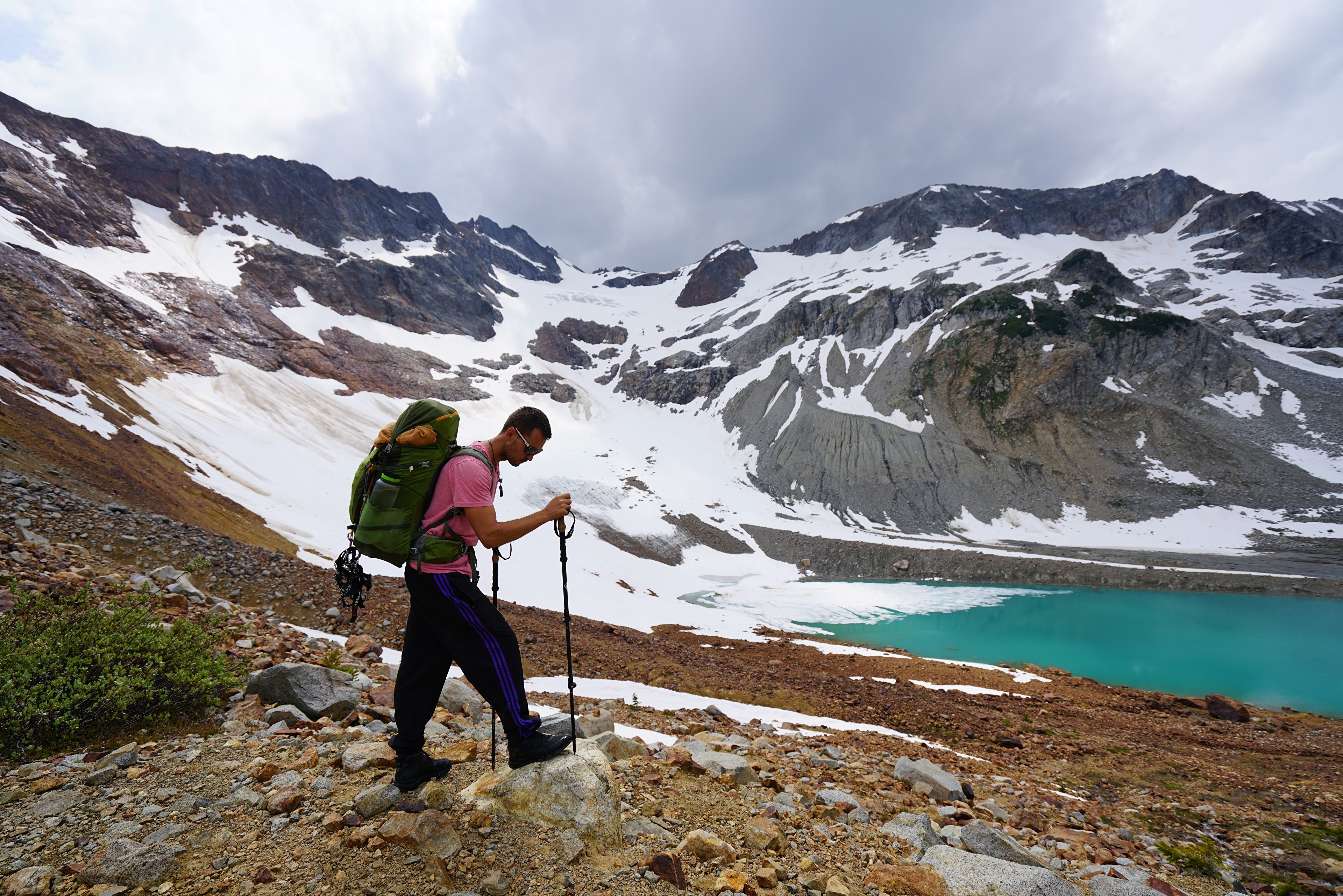 Man with backpack hiking near snowy mountains and lake HD Wallpaper