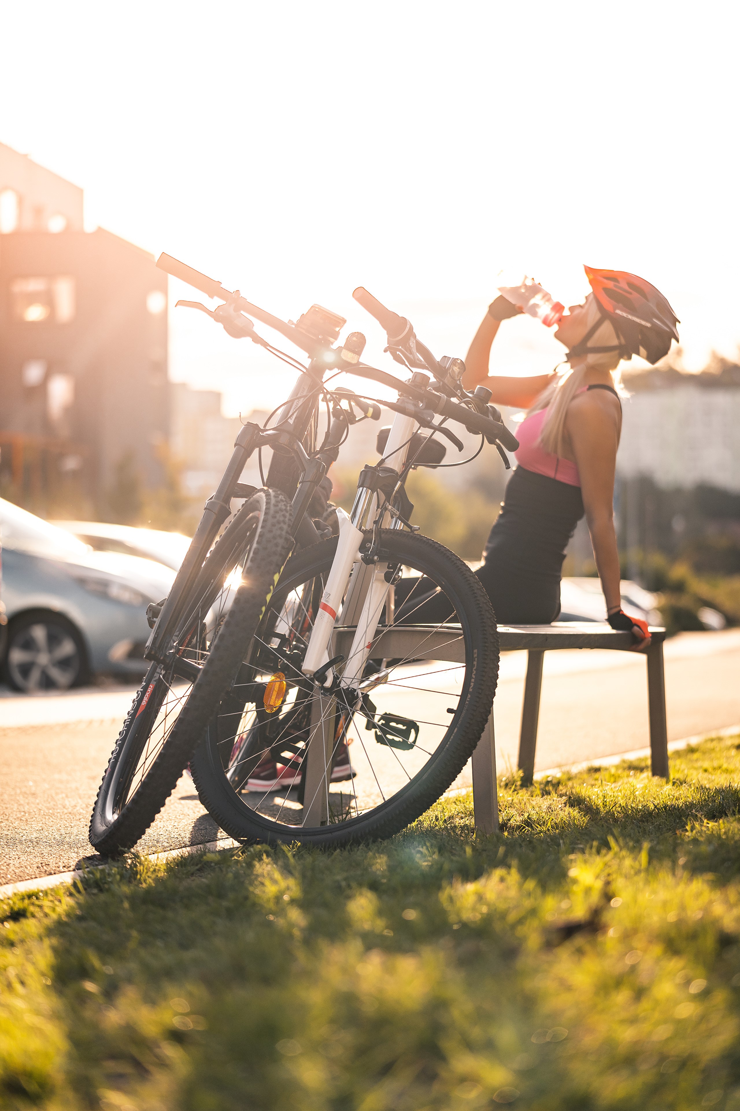 Woman in helmet drinking water next to bicycles HD Phone Wallpaper