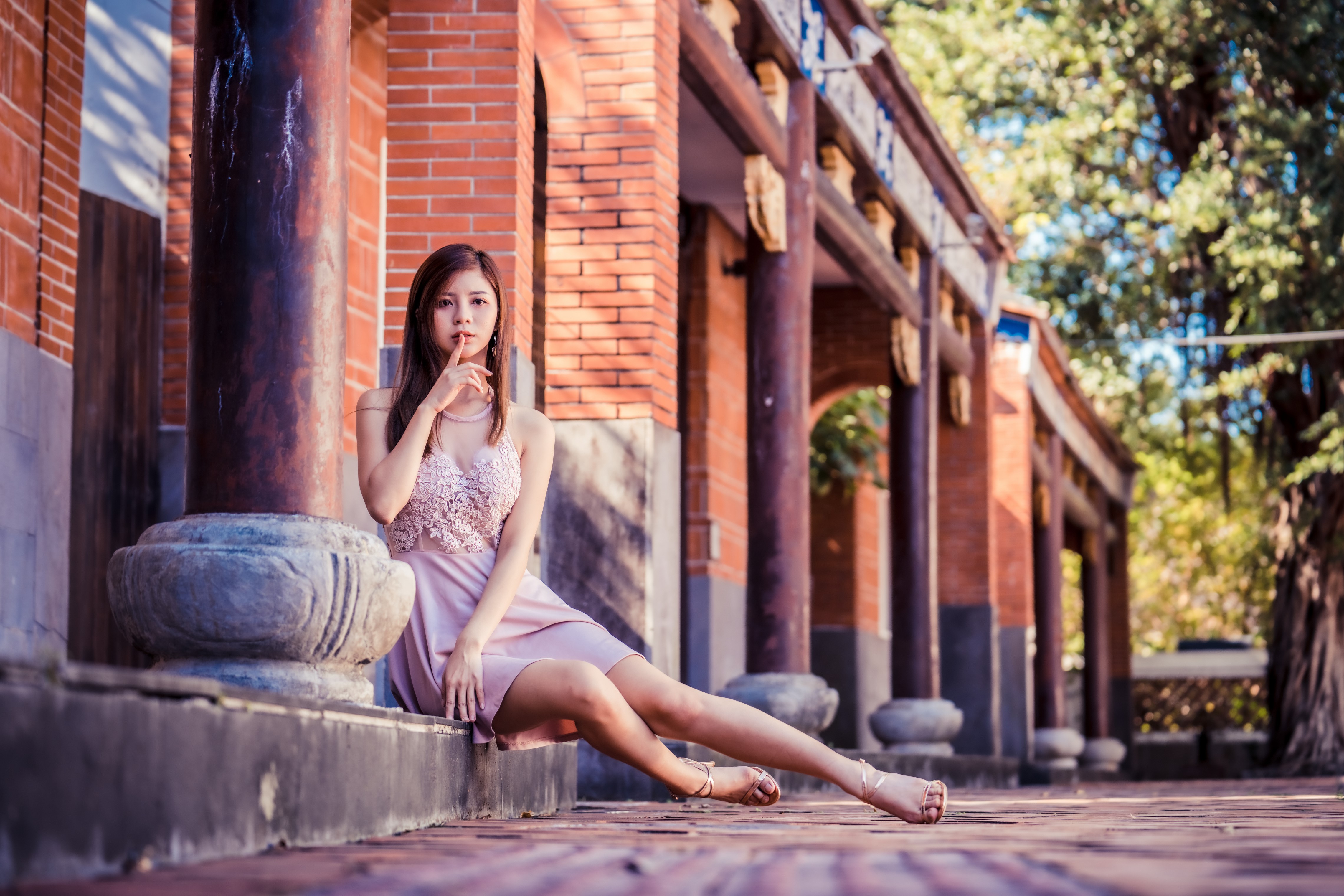 Asian woman sitting by a brick building HD Wallpaper