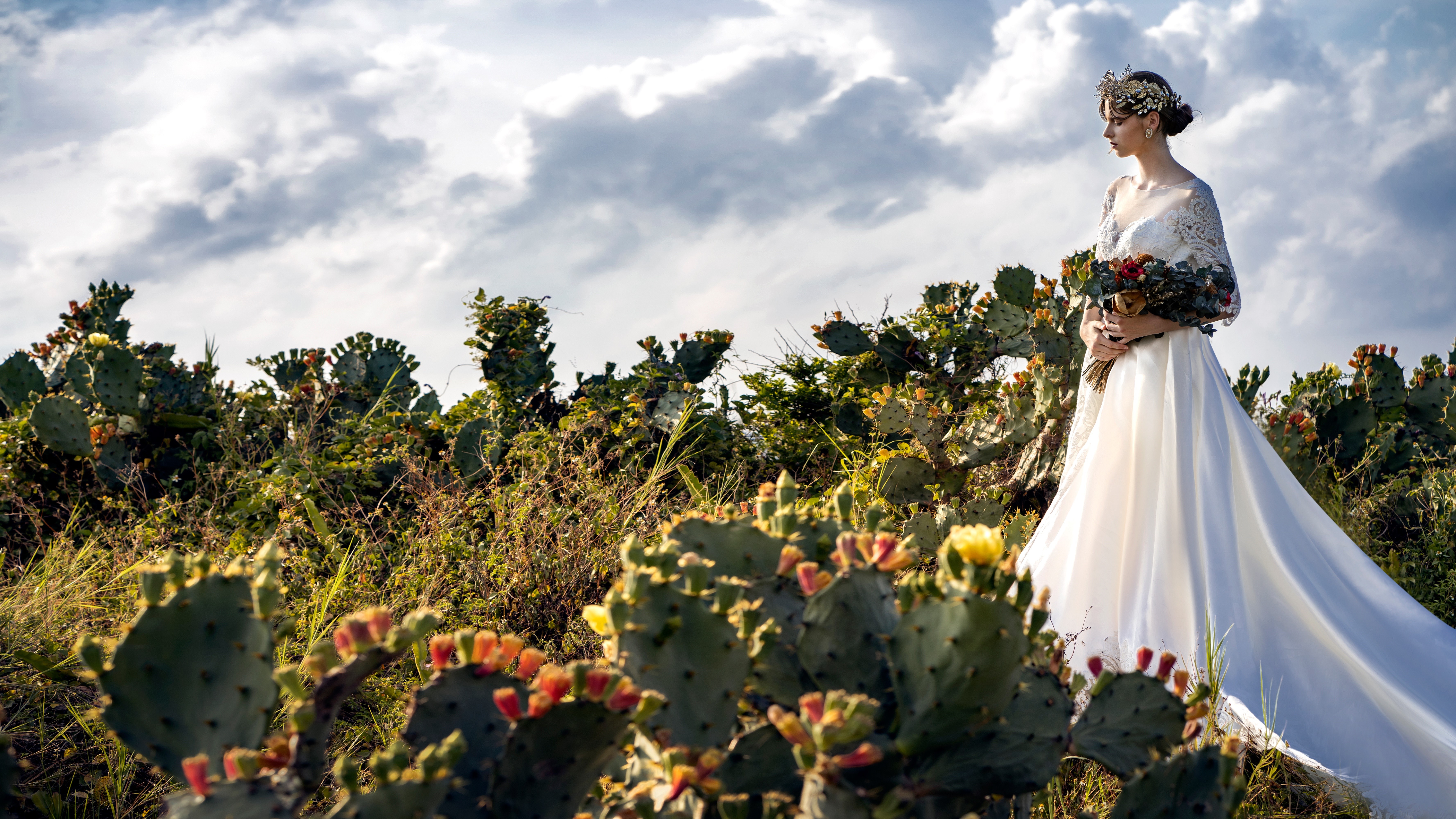 Bride in a wedding dress holding a bouquet in a cactus field HD Wallpaper