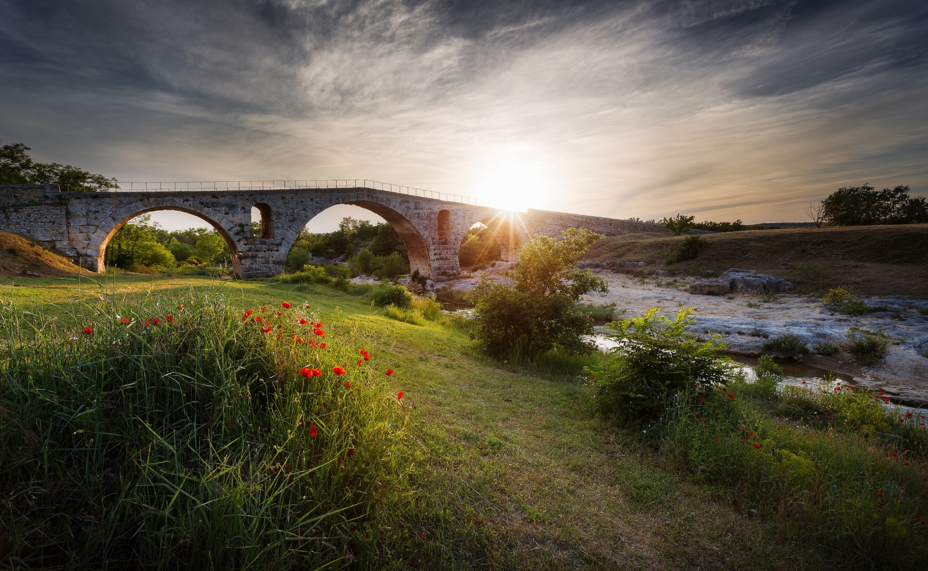Stone bridge over a stream at sunset with poppies HD Wallpaper