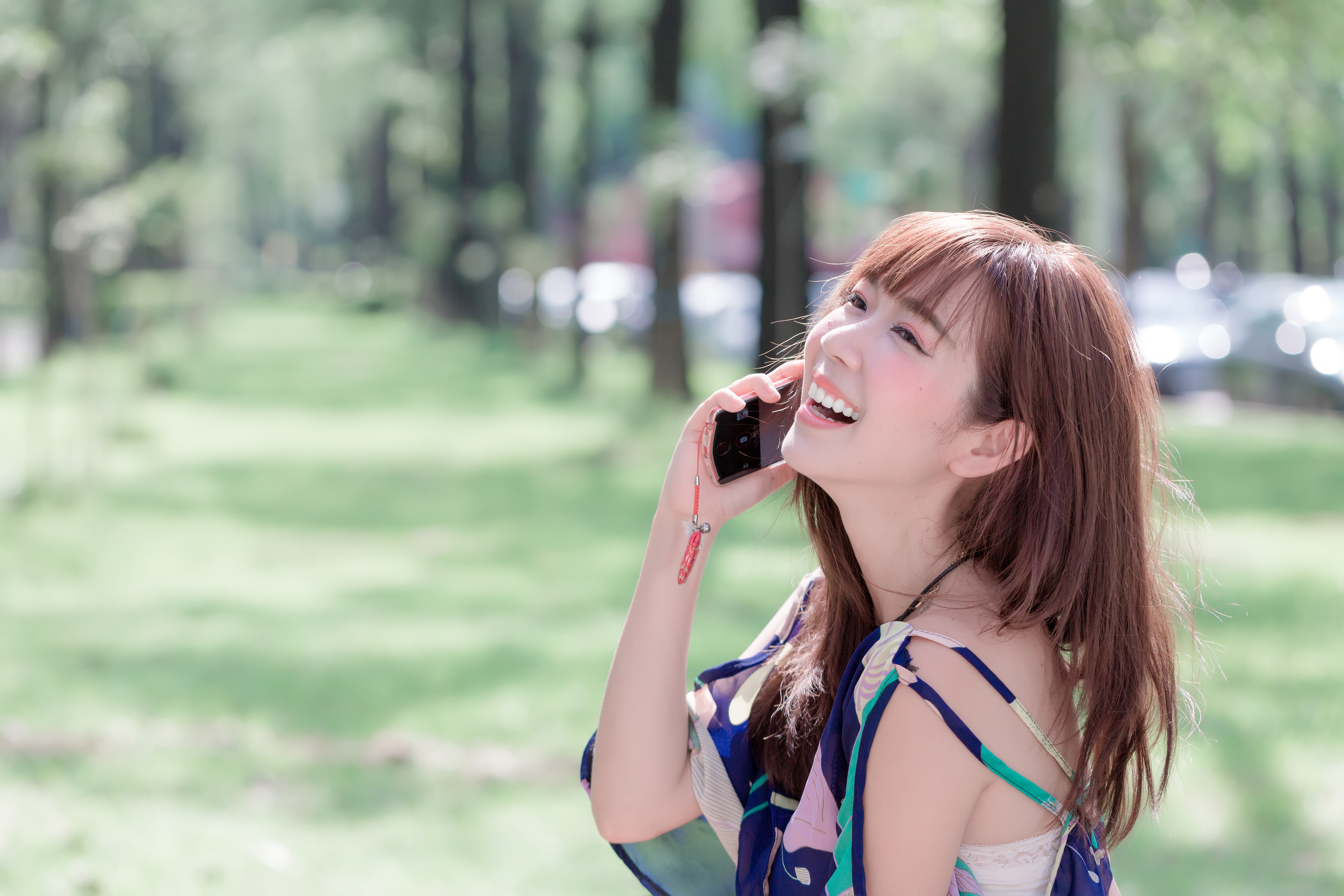 Asian woman laughing while on the phone in a park HD Wallpaper