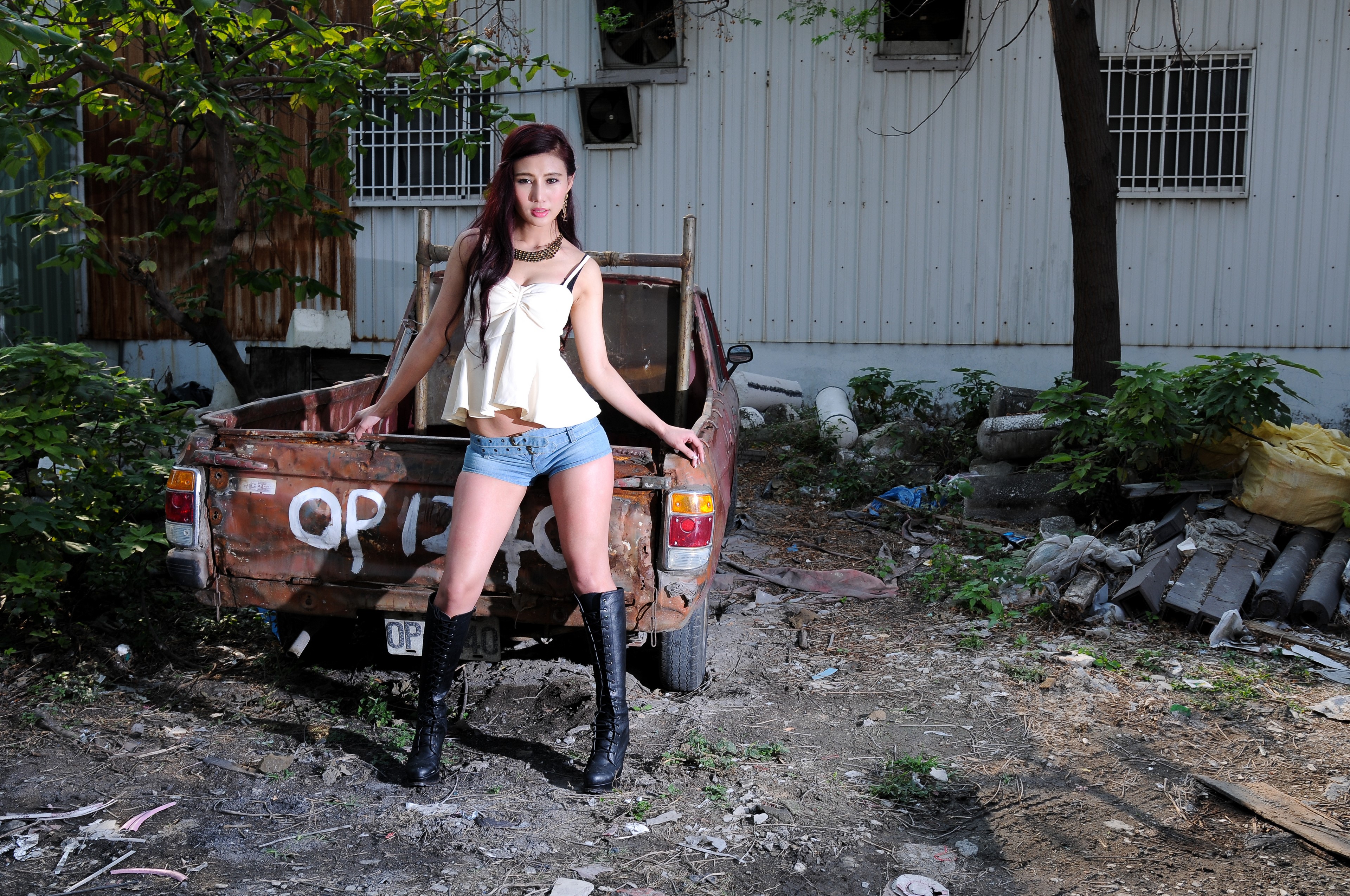 Asian woman in shorts and boots posing by a rusty truck HD Wallpaper