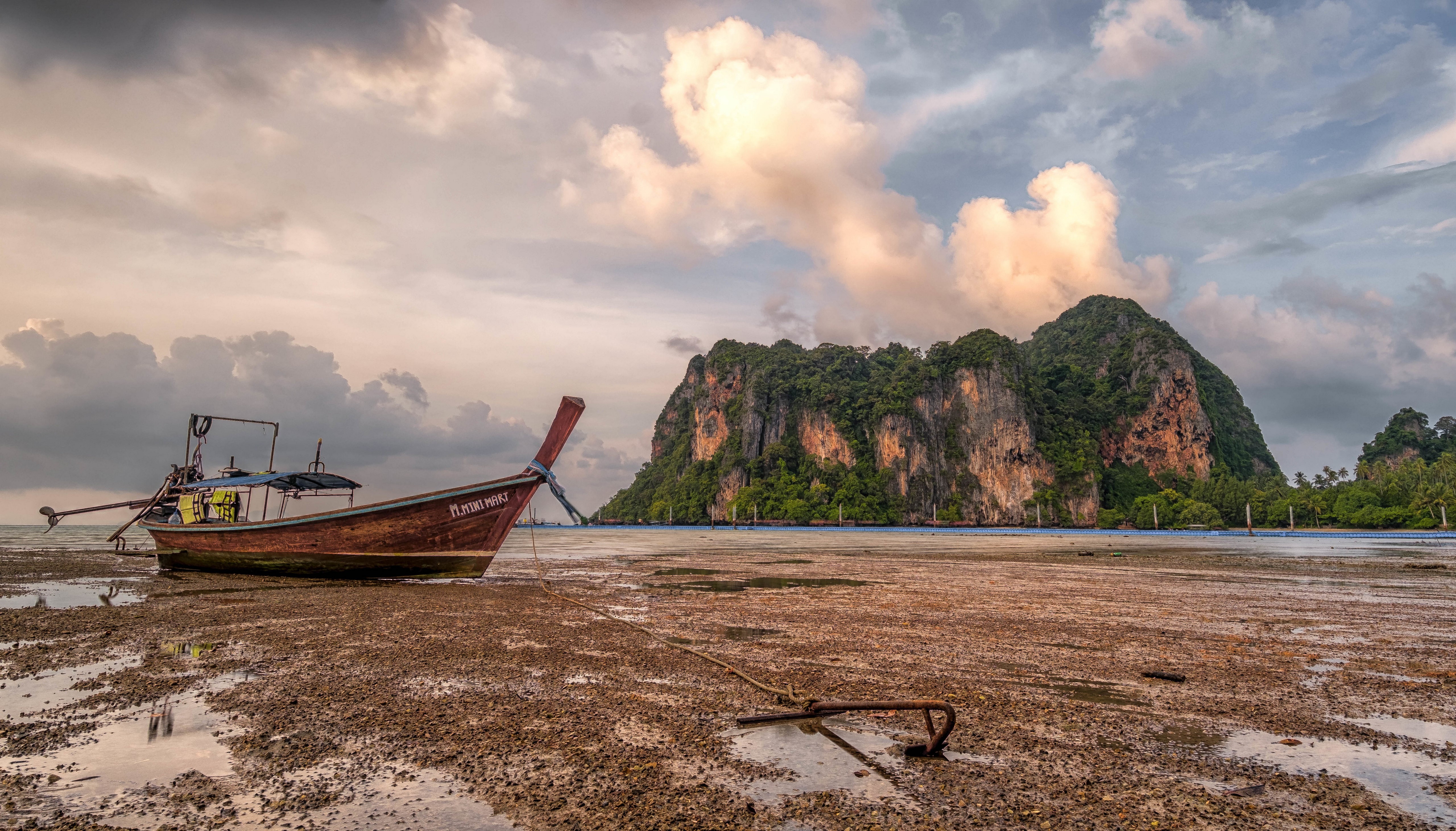 Longtail boat on a muddy shore with limestone cliffs in Krabi, Thailand HD Wallpaper