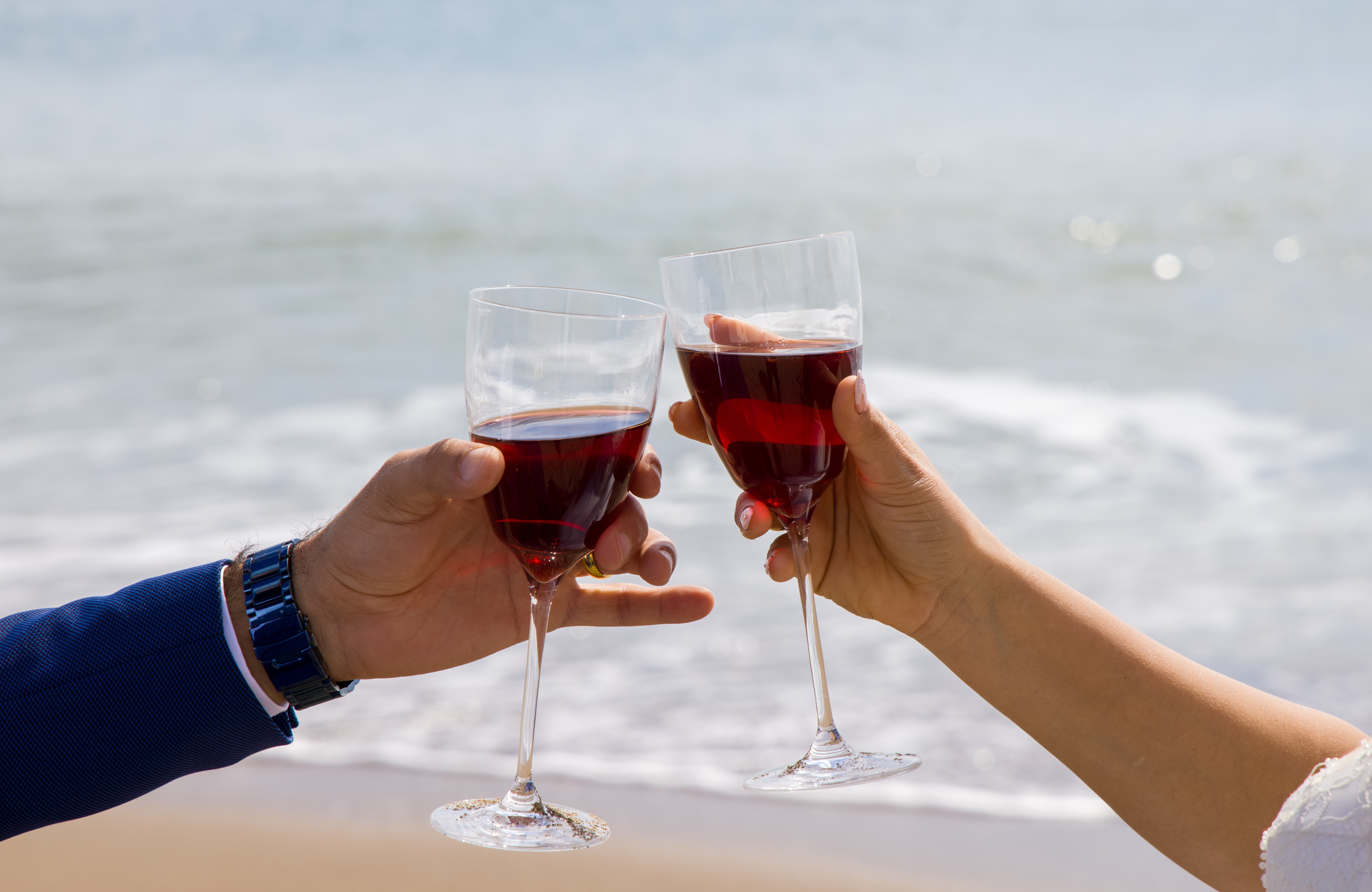 Hands toasting with red wine on the beach HD Wallpaper