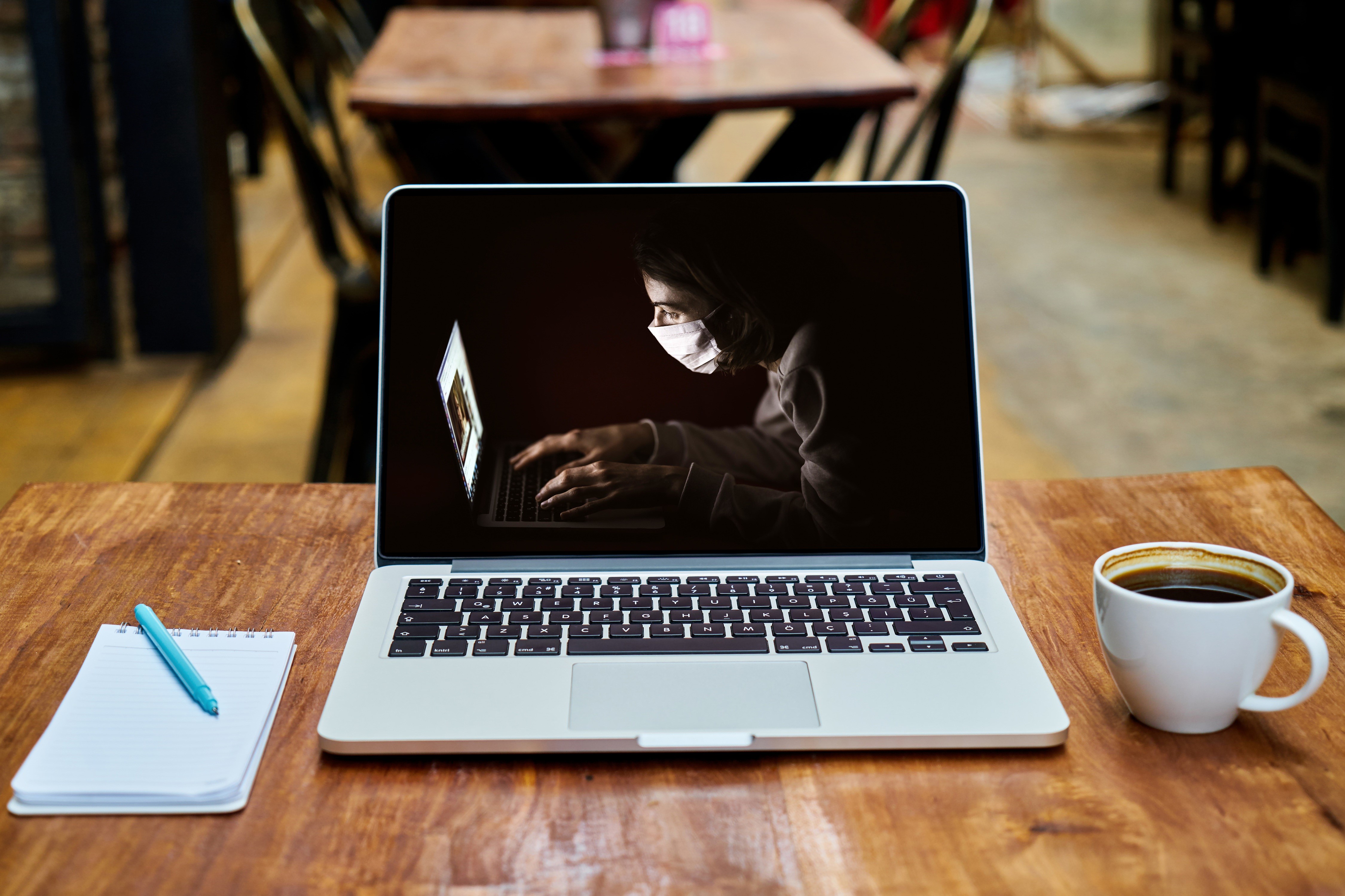 Laptop with person wearing mask, coffee, and notepad HD Wallpaper