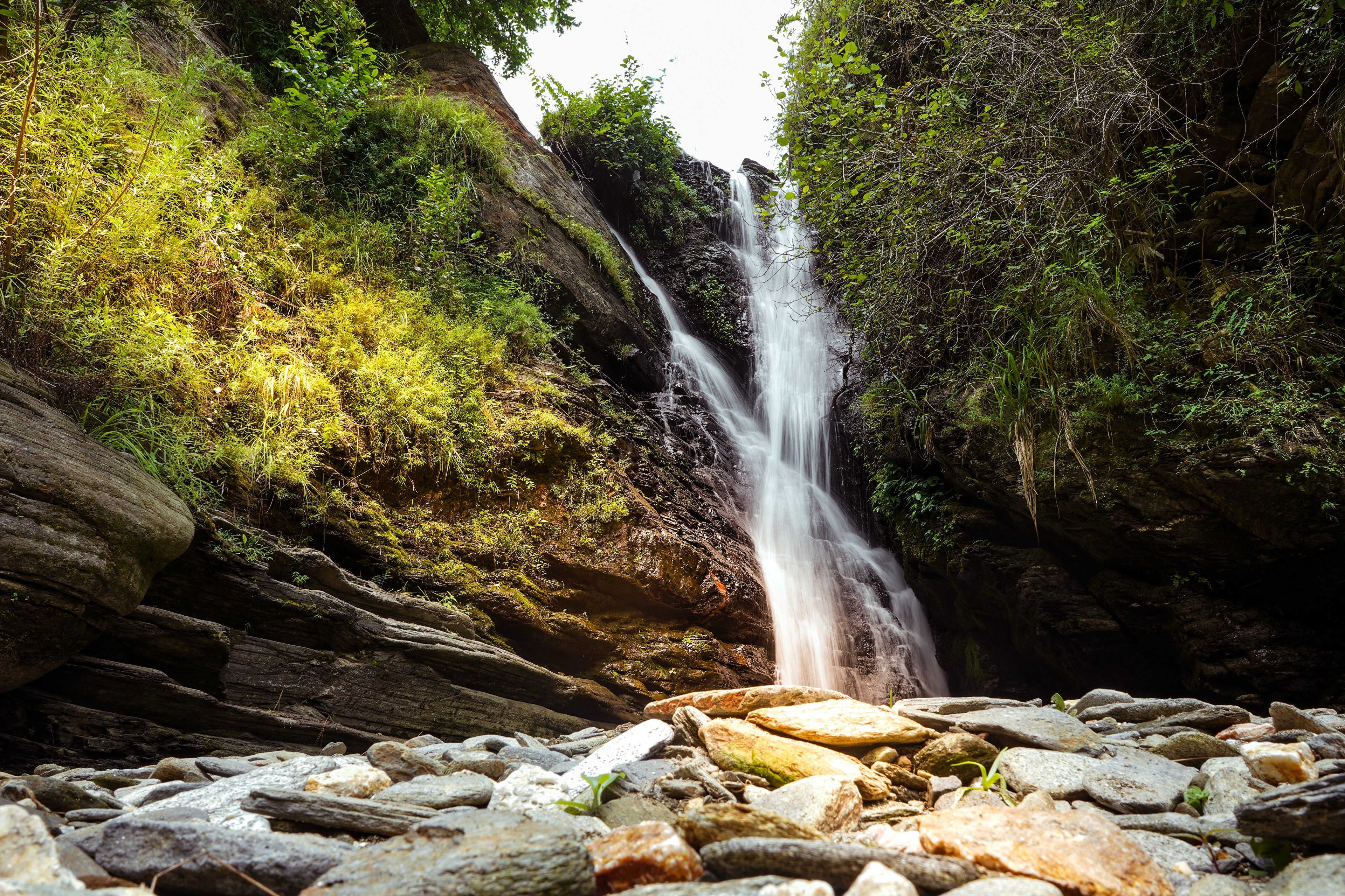 Waterfall cascading over rocks with surrounding greenery HD Wallpaper