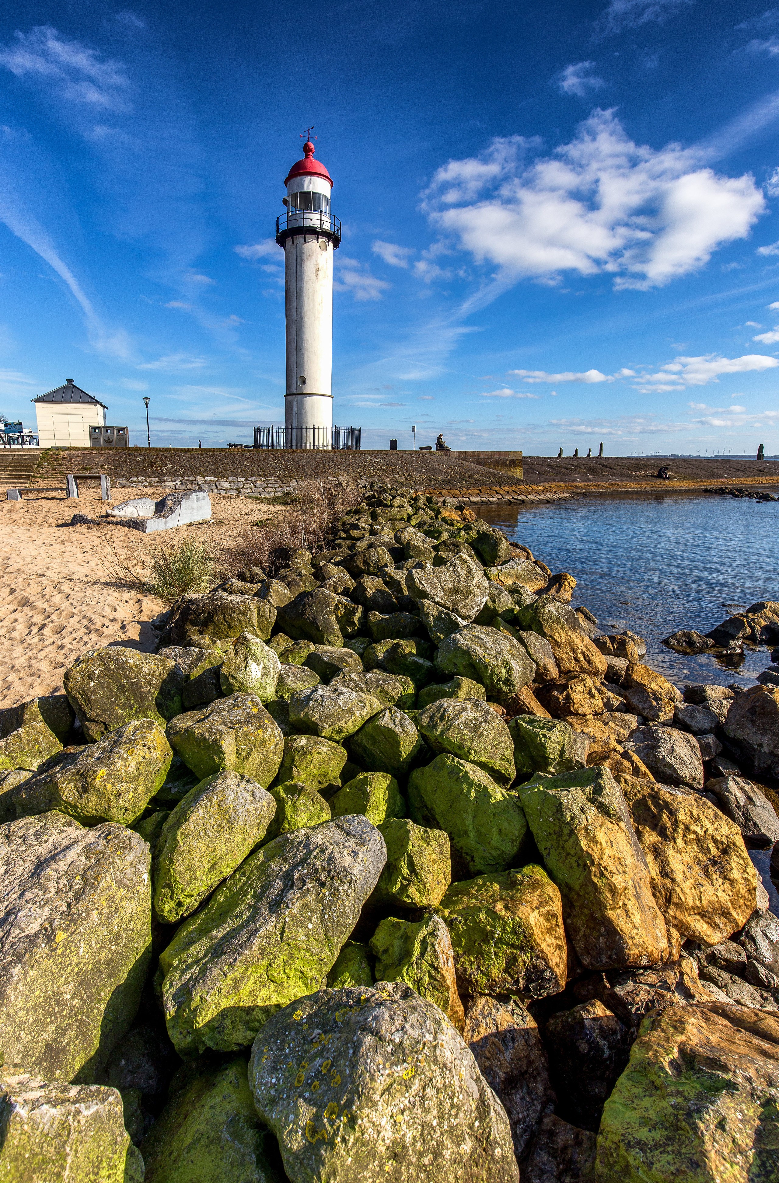 Lighthouse at Hellevoetsluis, Netherlands with rocky shore HD Phone Wallpaper