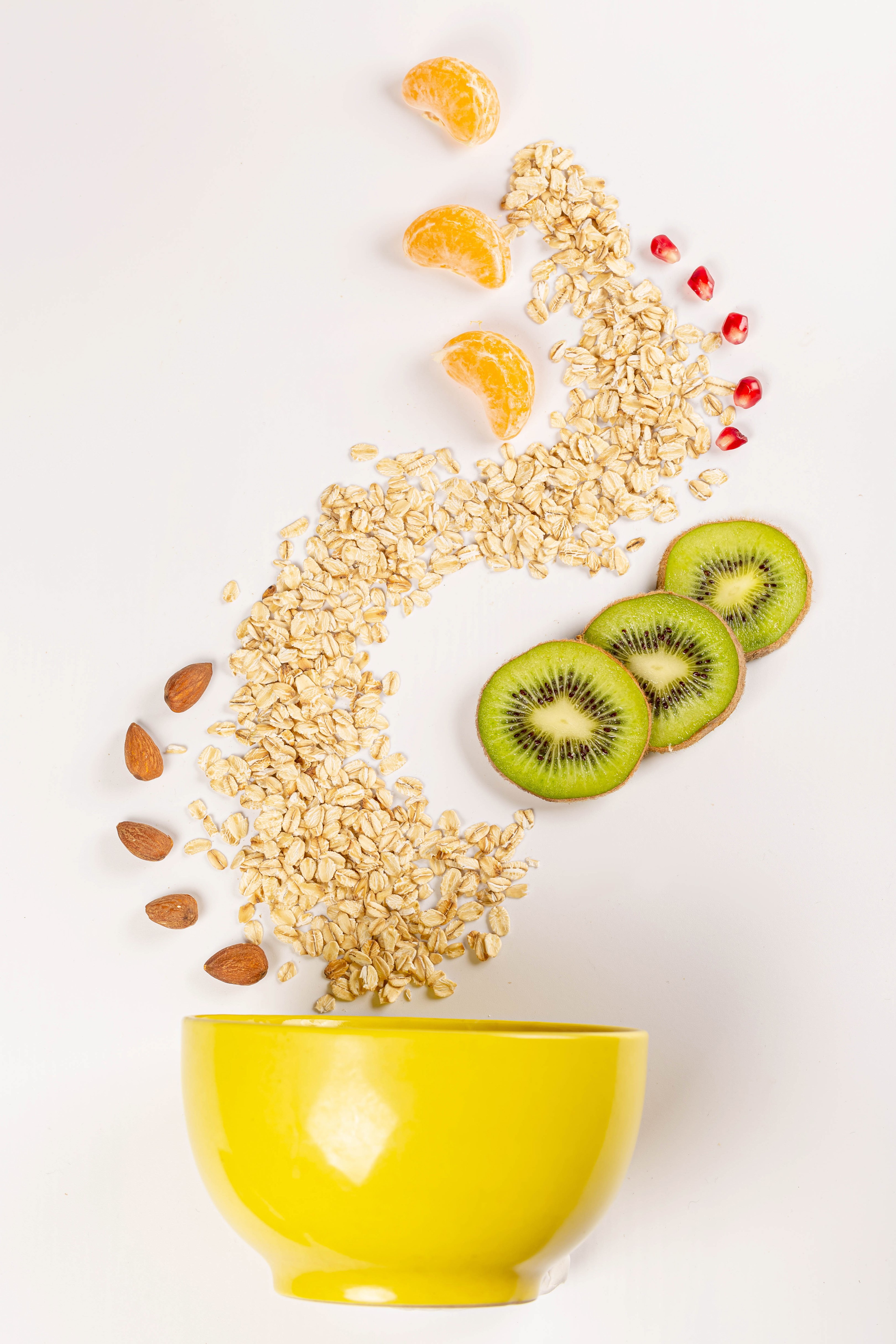 Oatmeal with kiwi, tangerine, almonds, and pomegranate seeds in a yellow bowl HD Phone Wallpaper