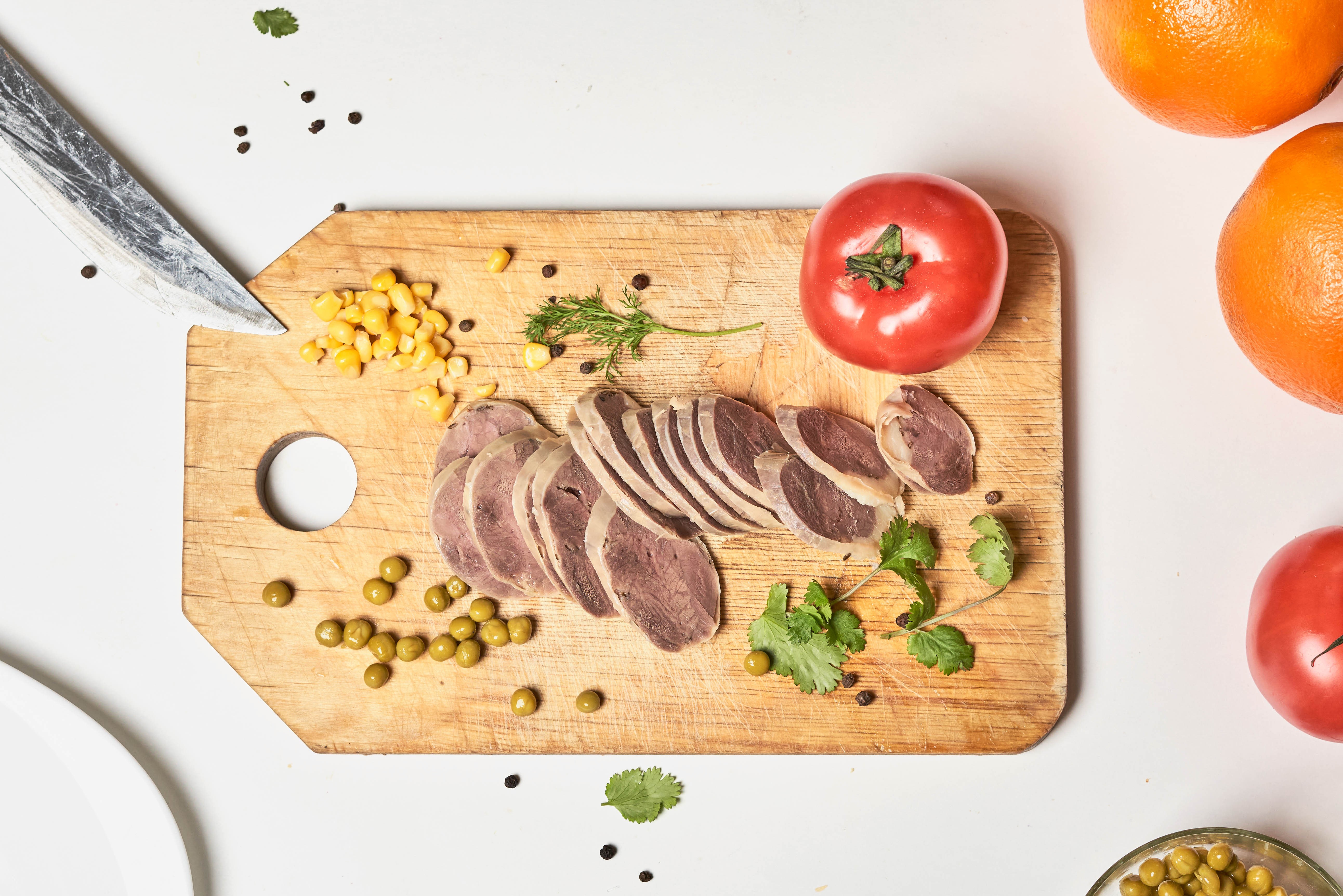 Sliced meat on cutting board with tomatoes and oranges HD Wallpaper