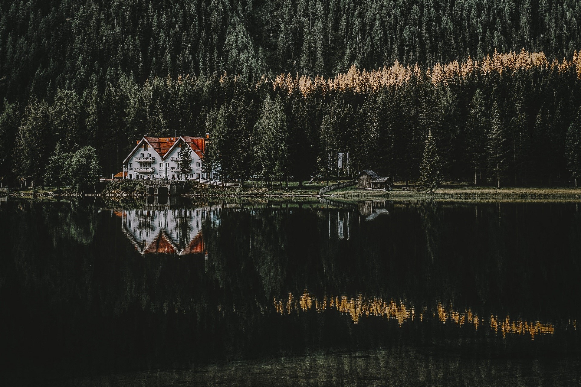 White house with red roof reflected in a dark lake surrounded by a forest HD Wallpaper