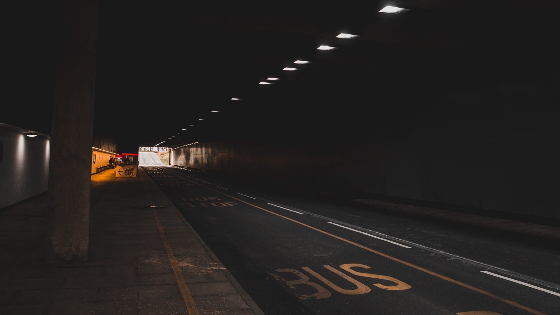 Dark tunnel with bus stop and road markings HD Wallpaper