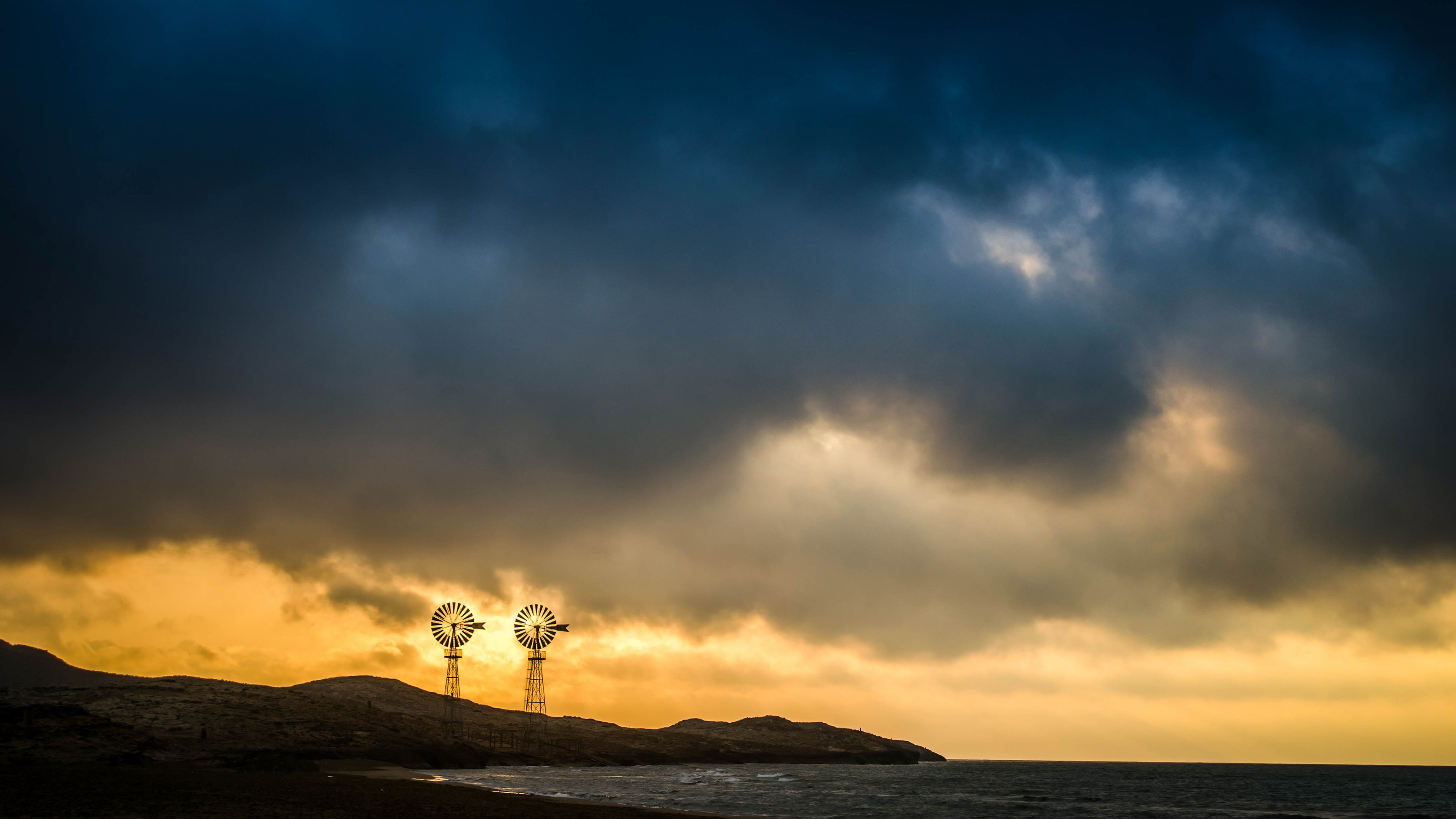 Two windmills on a rocky coast at sunset HD Wallpaper