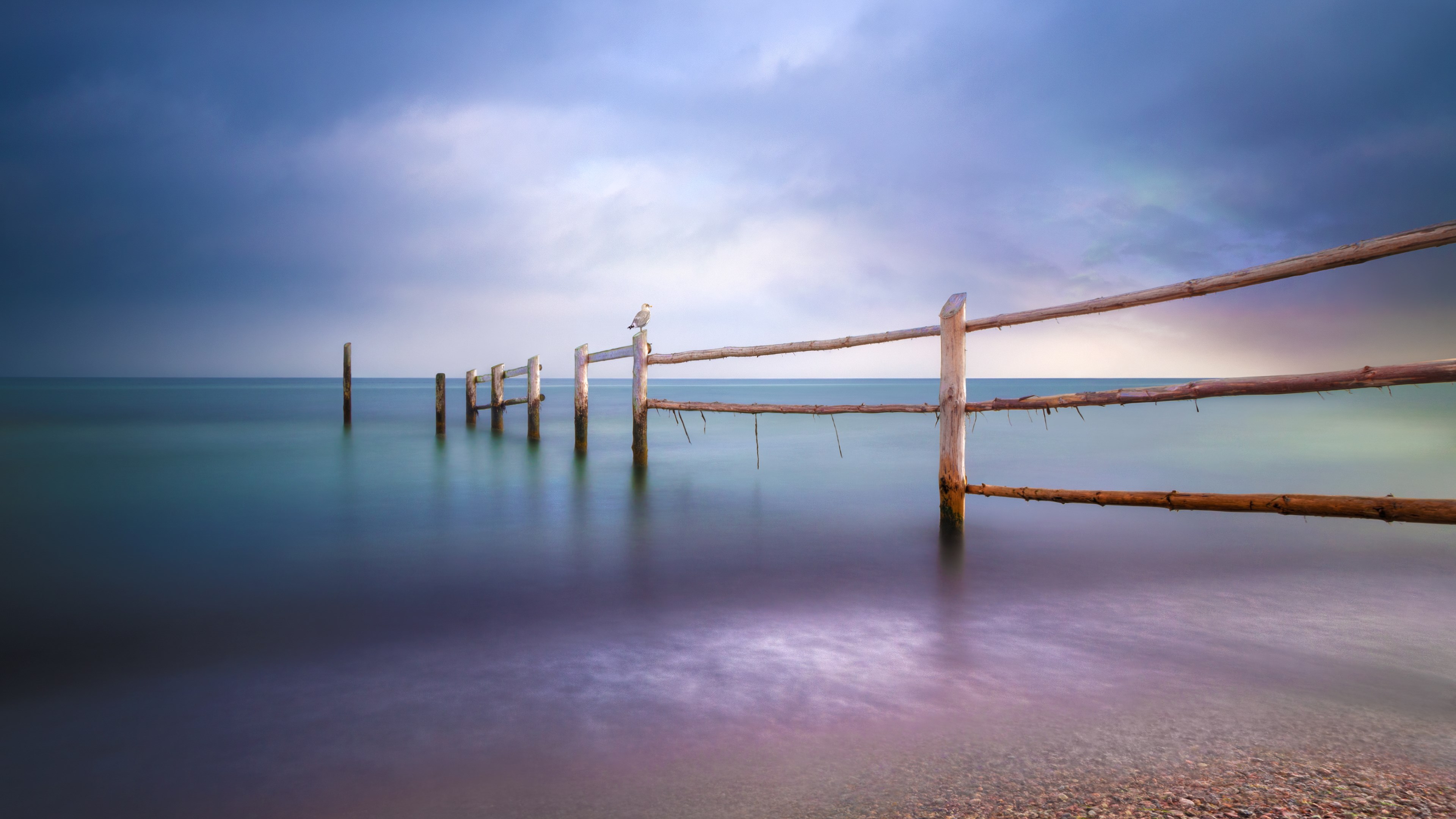 Wooden fence posts in the ocean under a cloudy sky HD Wallpaper