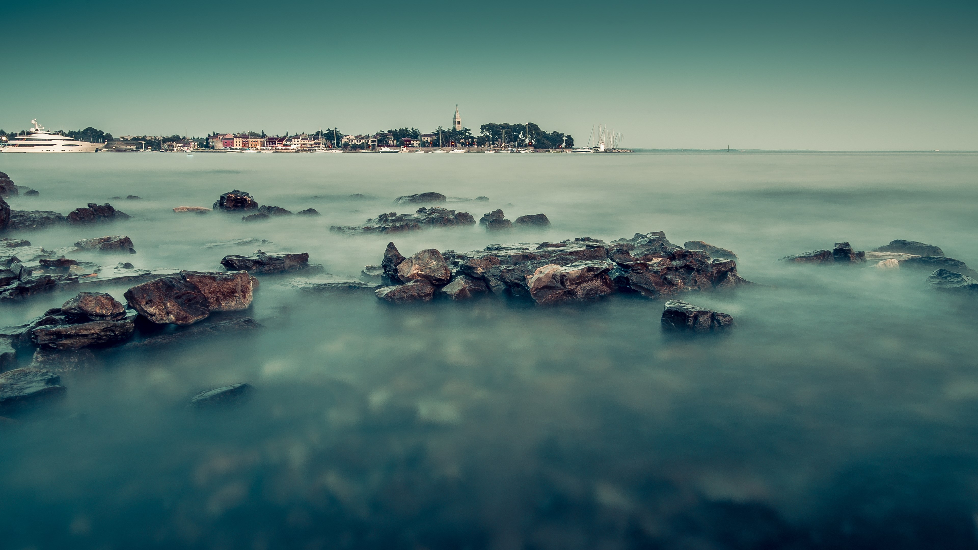Rocky coastline with a town and yachts in the distance HD Wallpaper
