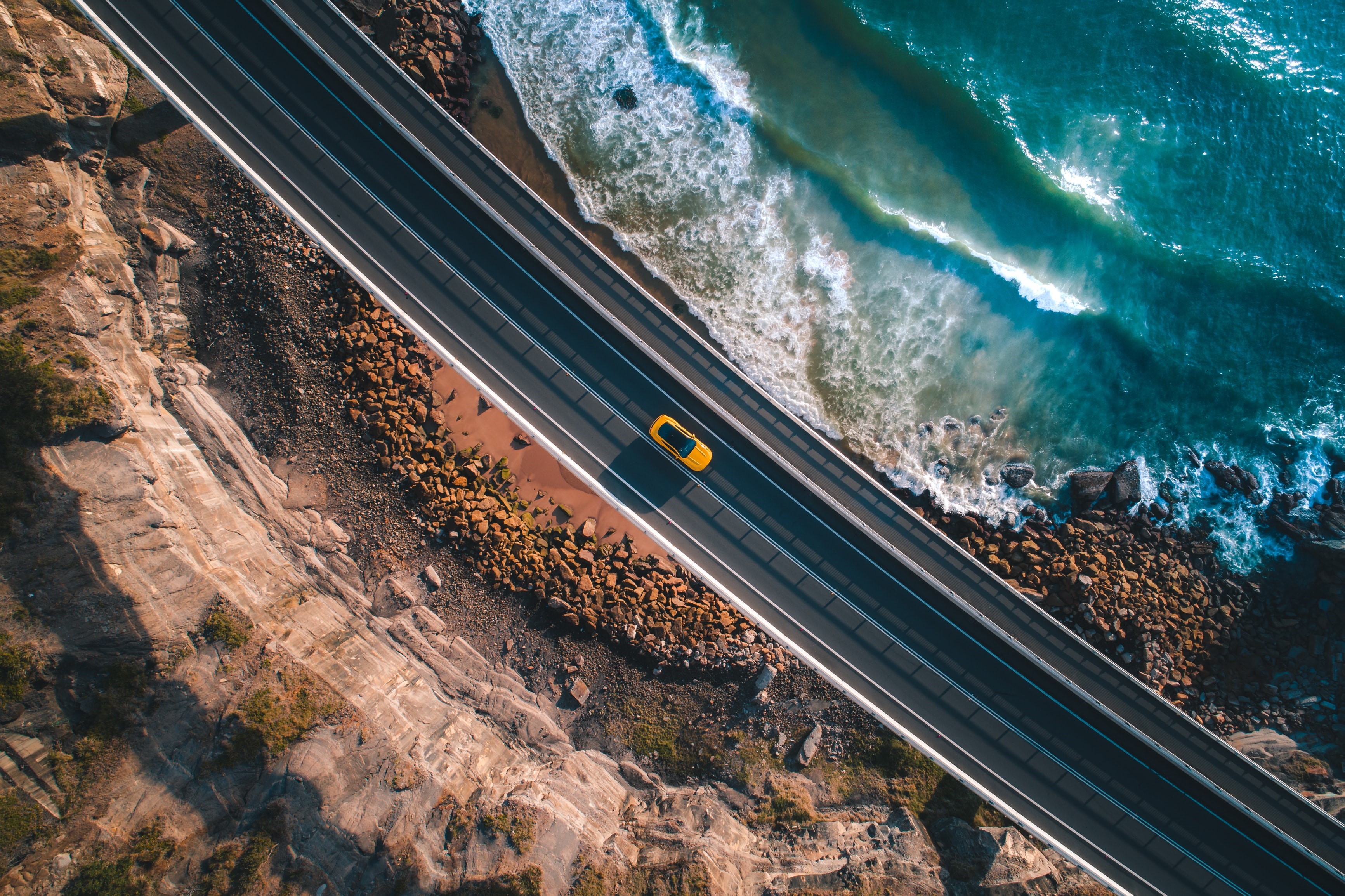 Yellow car driving on a coastal road HD Wallpaper