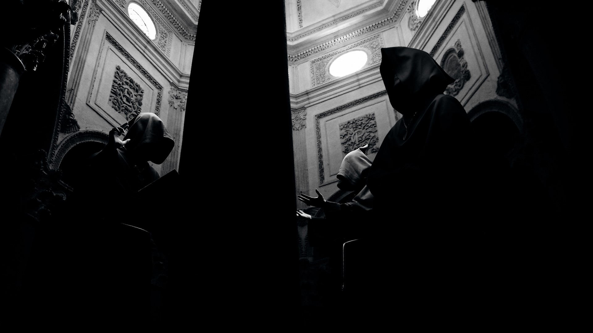 Monks in cloaks in a dimly lit ornate building HD Wallpaper