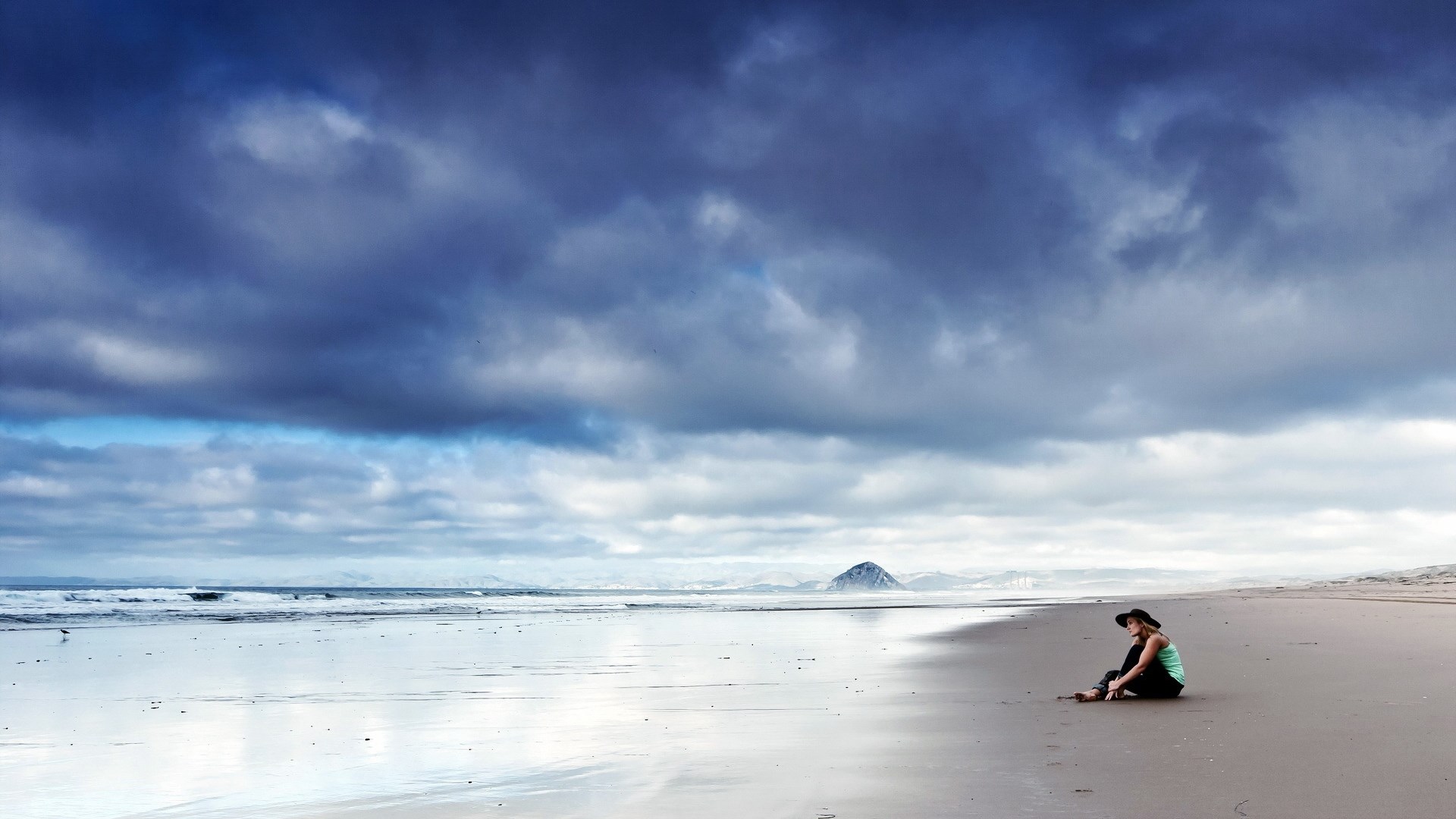Woman sitting on a beach under stormy clouds HD Wallpaper