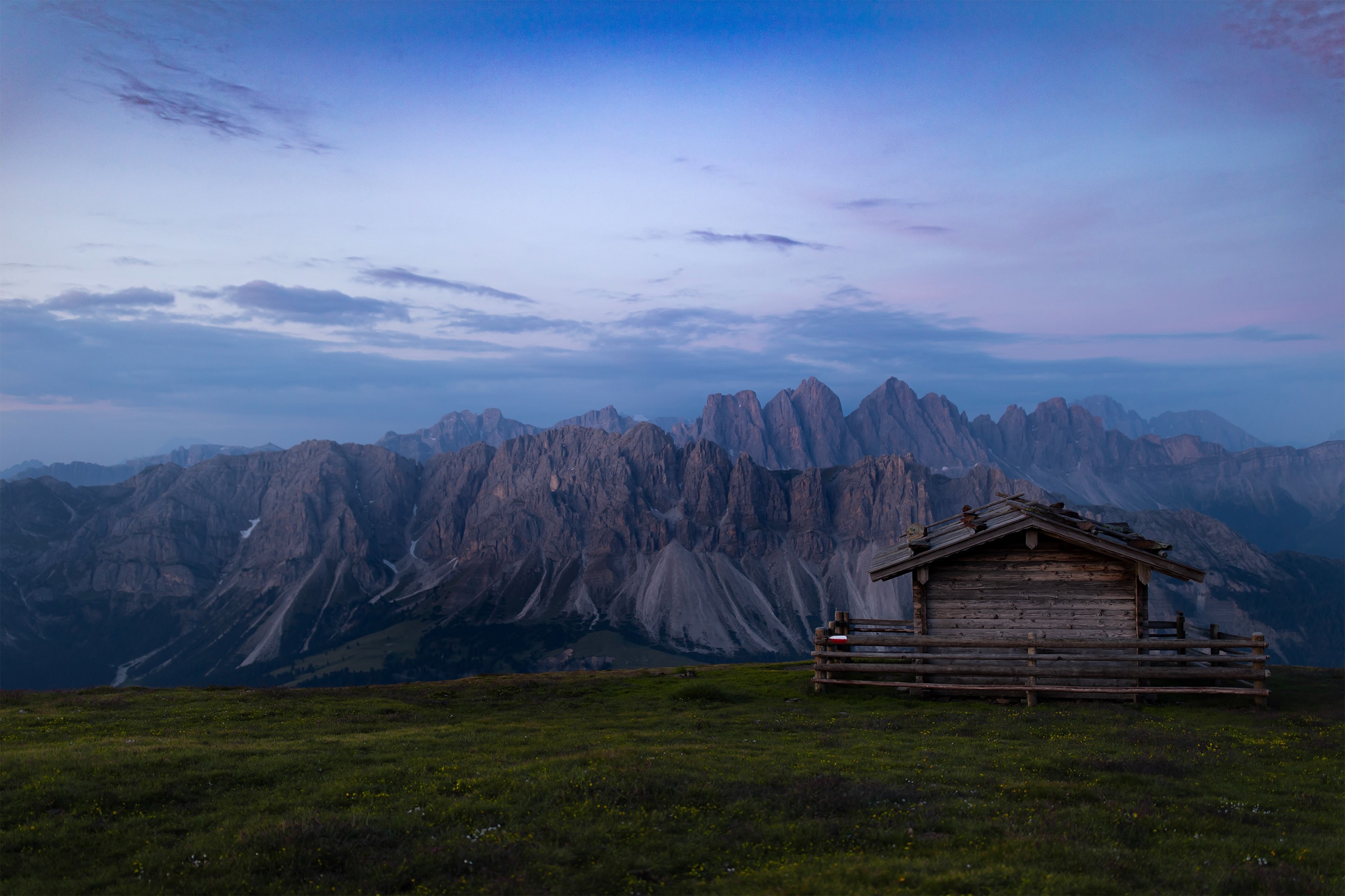 Wooden cabin on a grassy hill with mountains and clouds HD Wallpaper