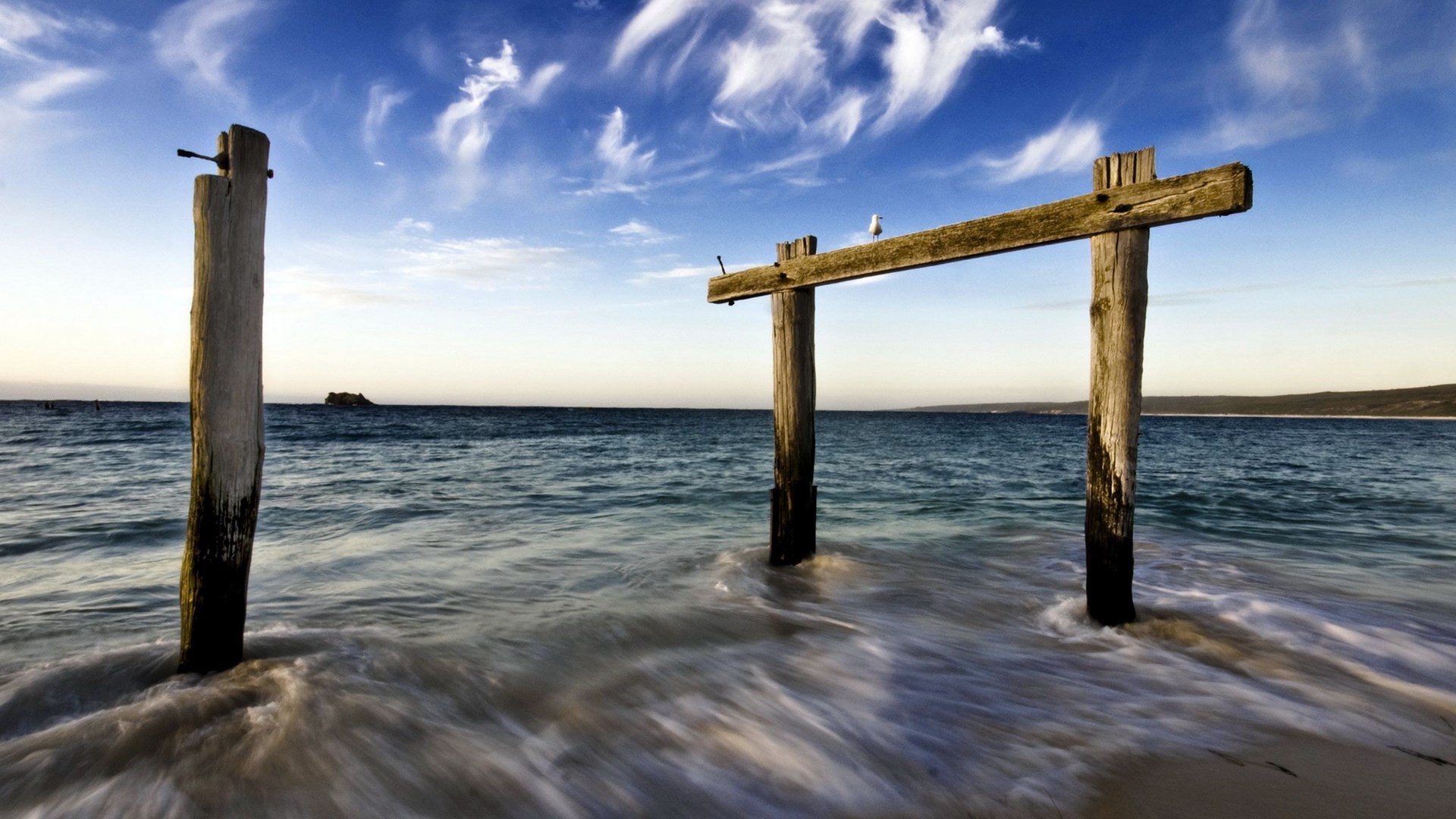 Wooden posts and a beam on a beach with ocean waves HD Wallpaper